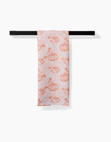 The Pumpkin Field white tea towel by Charlie Rowan Designs, featuring an orange pumpkin pattern and made from recycled materials, is neatly folded over a black towel bar against a plain white background.