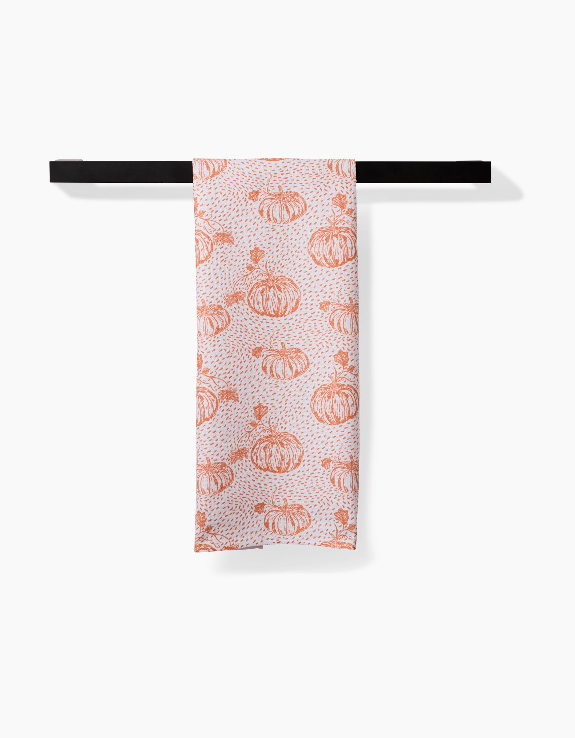 The Pumpkin Field white tea towel by Charlie Rowan Designs, featuring an orange pumpkin pattern and made from recycled materials, is neatly folded over a black towel bar against a plain white background.