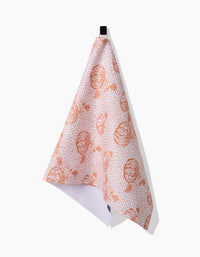 The Charlie Rowan Designs Pumpkin Field white kitchen towel, made from recycled materials, features orange pumpkin and foliage patterns and hangs from a black loop against a white background.