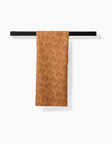 The Pumpkin Patchwork recycled kitchen towel by Aubrey Fairchild, featuring outlined pumpkins, hangs neatly over a black towel bar against a white background.