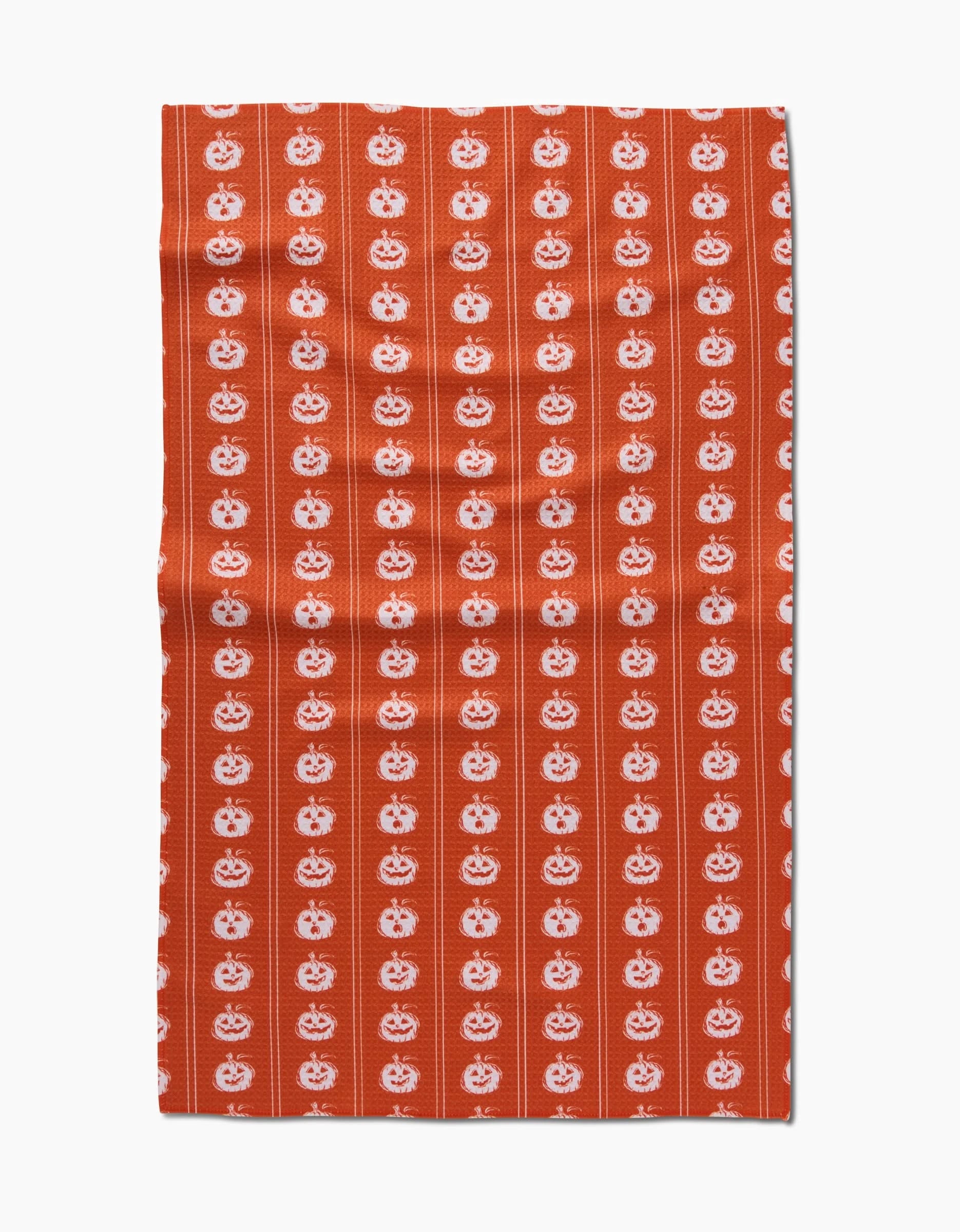 The Pumpkin Pinstripes kitchen towel by Aubrey Fairchild is orange, made from recycled materials, and features vertical stripes of white jack-o-lantern faces with subtle thin lines in the background.