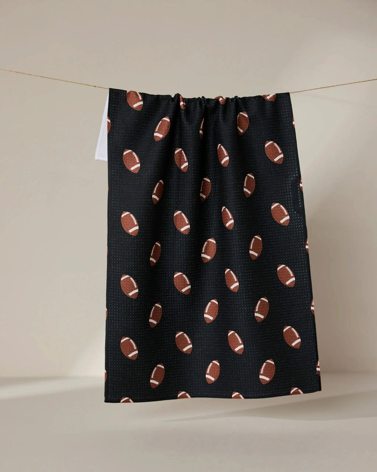 The GEOMETRY Quarter Back is a black tea towel made from recycled materials, decorated with brown and white football patterns, and shown hanging against a neutral background.