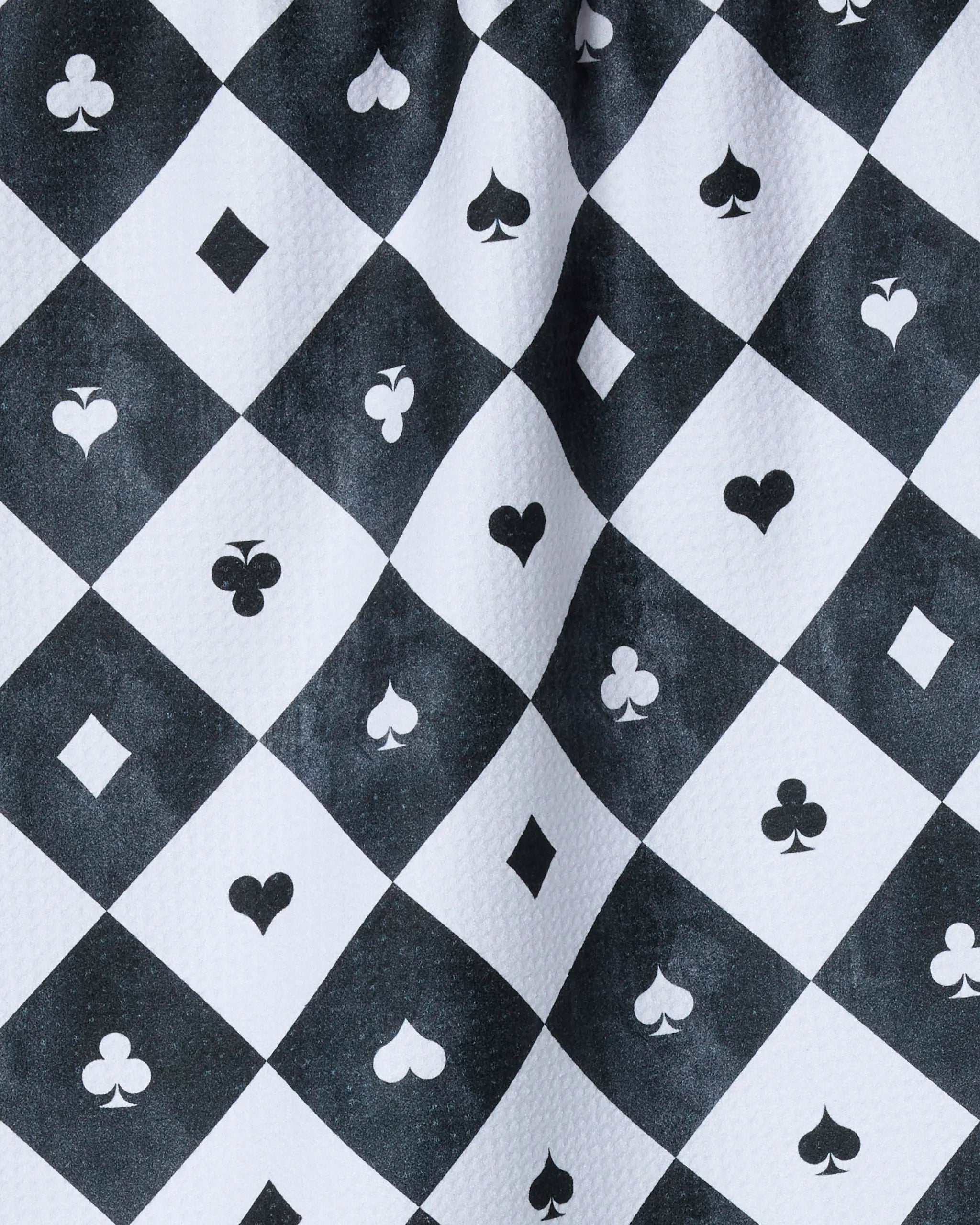 Geometry’s "Queen of Everything" kitchen towel features a black and white checkered pattern with diamond shapes, each displaying a hearts, clubs, spades, or diamonds card suit—printed on recycled materials with subtle fold details.