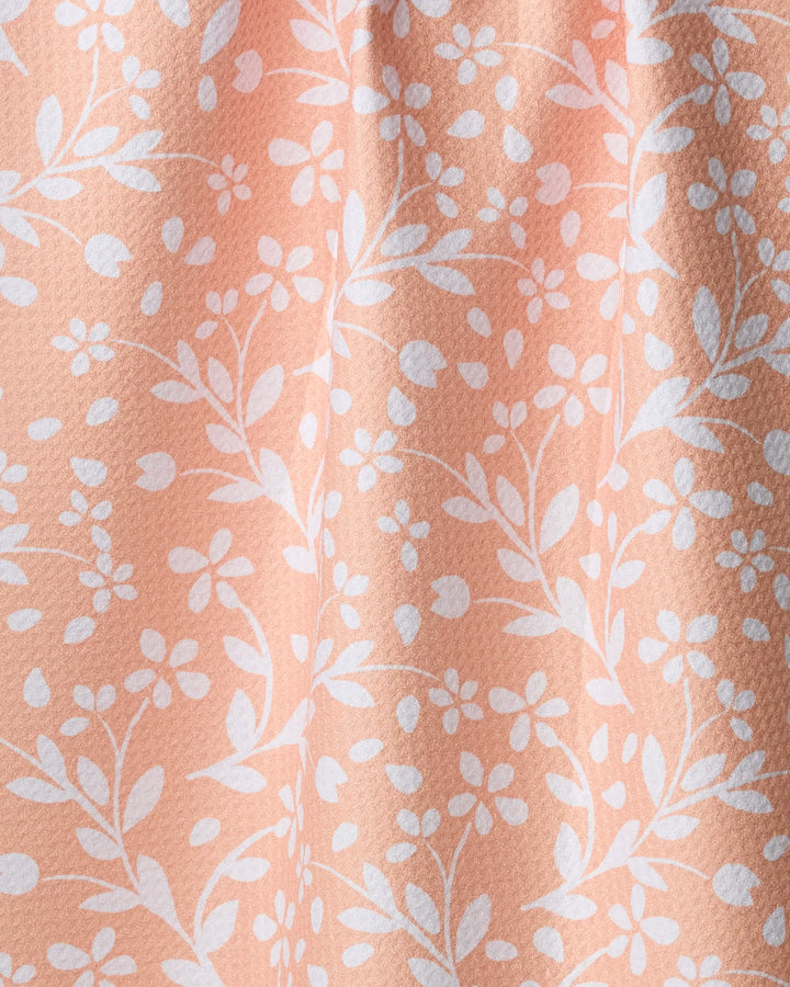 Close-up of Geometry’s “Quiet Radiance” tea towel, crafted from recycled Geoweave fabric in a peach hue with white floral and leaf designs. Its soft, textured surface and gentle folds create an elegant, delicate look.