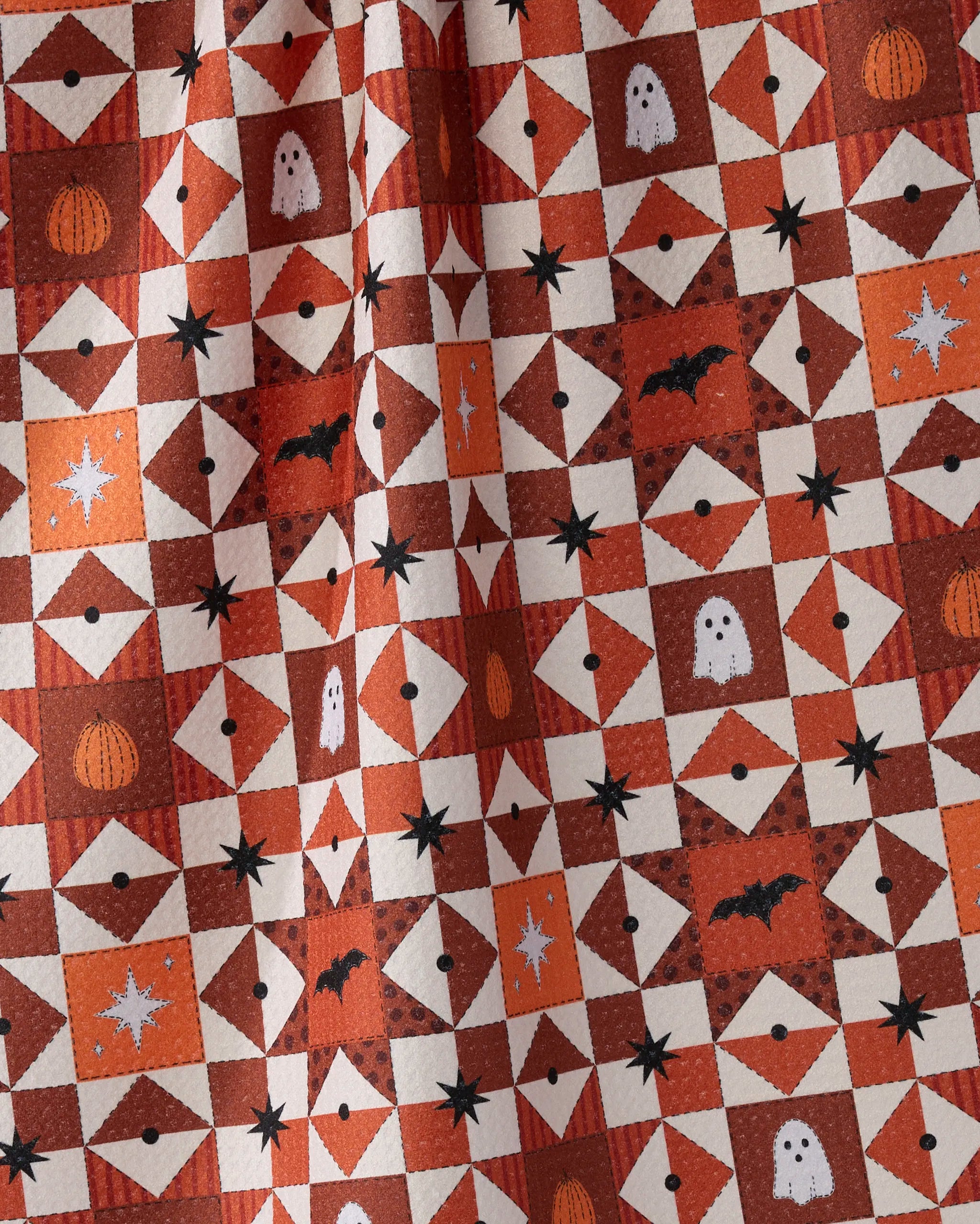 The Geometry Quilt Work tea towel features a symmetrical orange and white Halloween pattern with pumpkins, ghosts, bats, stars, and geometric shapes. Festive and eco-friendly, it's made from recycled materials.