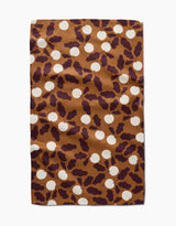 A rectangular brown Radishes kitchen tea towel by Lizzie Clark features white circles and dark purple abstract leaf shapes. The slightly wrinkled towel is displayed on a white background.