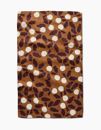 A rectangular brown Radishes kitchen tea towel by Lizzie Clark features white circles and dark purple abstract leaf shapes. The slightly wrinkled towel is displayed on a white background.