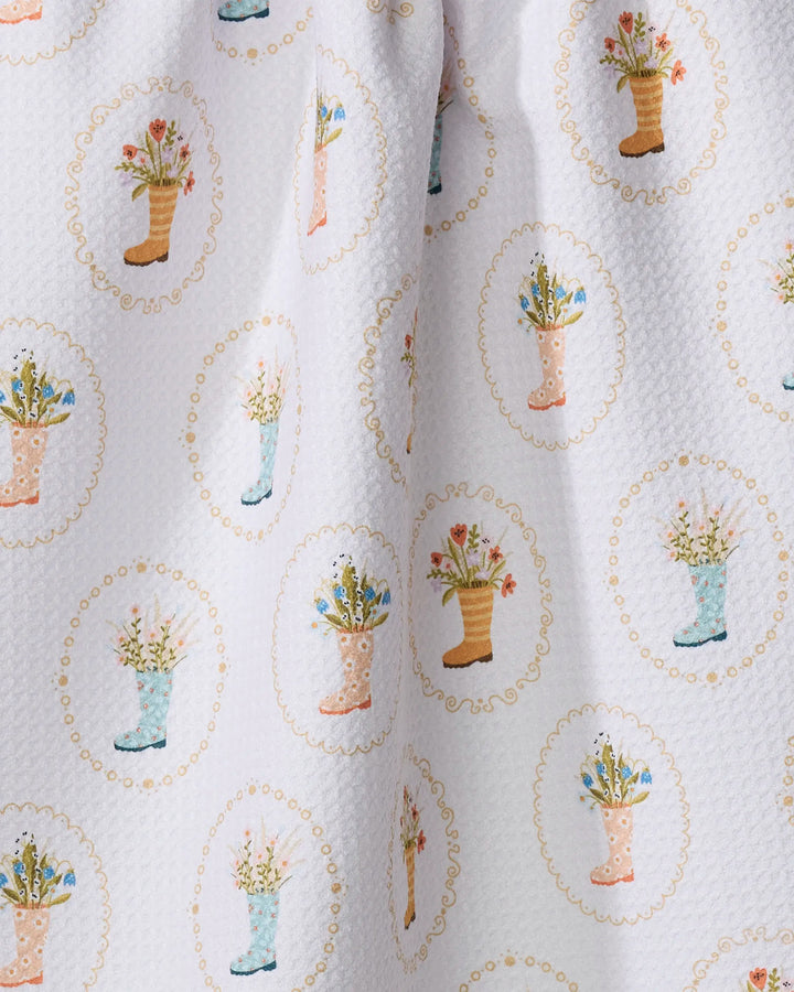 Rainboots in Bloom by Sara Mari is a white textured tea towel with pastel rain boots filled with flowers, each in an oval scalloped border. Made from recycled materials, this quick-drying towel adds color to your kitchen.