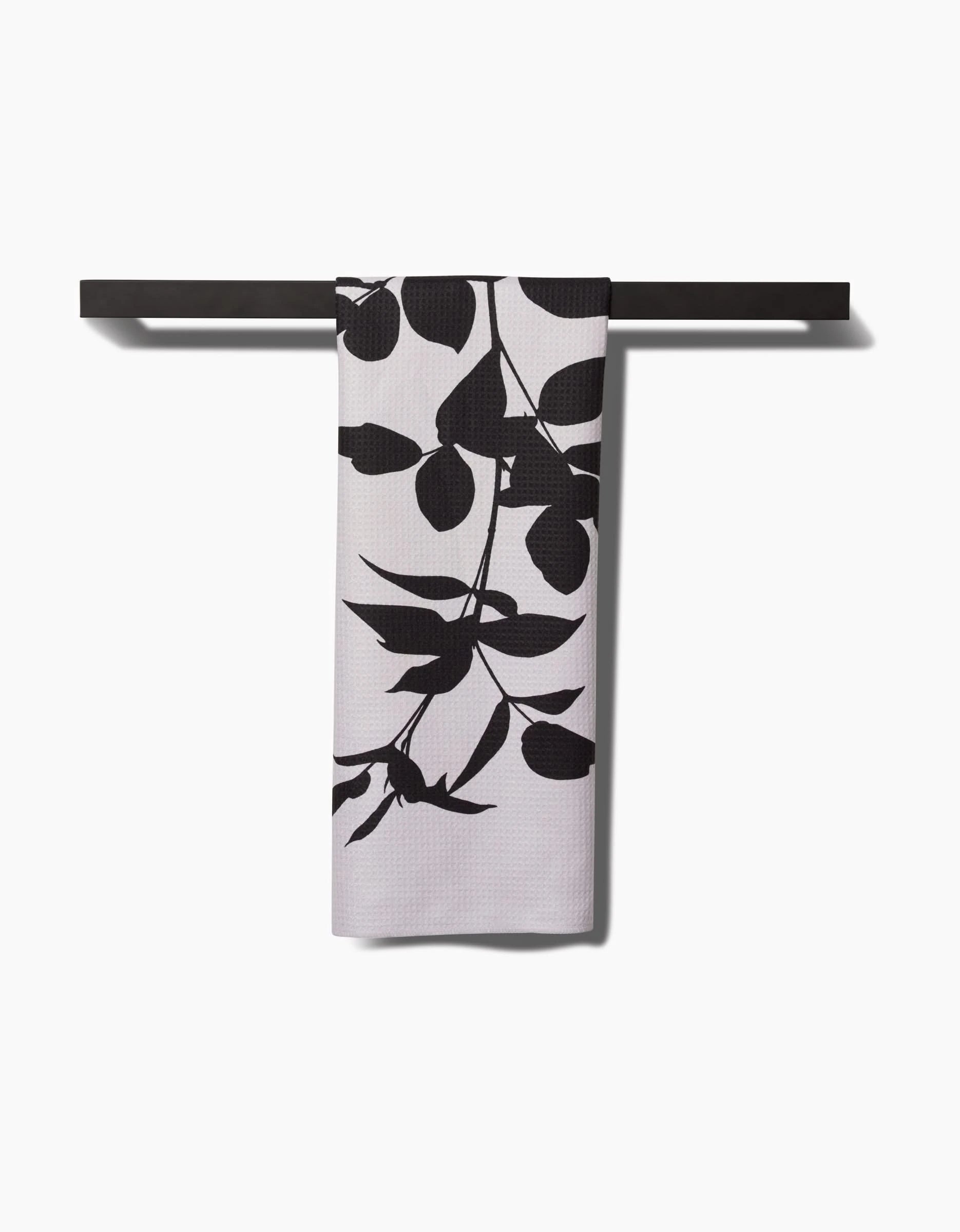 A PrintedPlant Raspberry tea towel with a bold black botanical leaf pattern hangs on a sleek black bar against a white background. Made from Geoweave™ fabric for superior absorbency and style.
