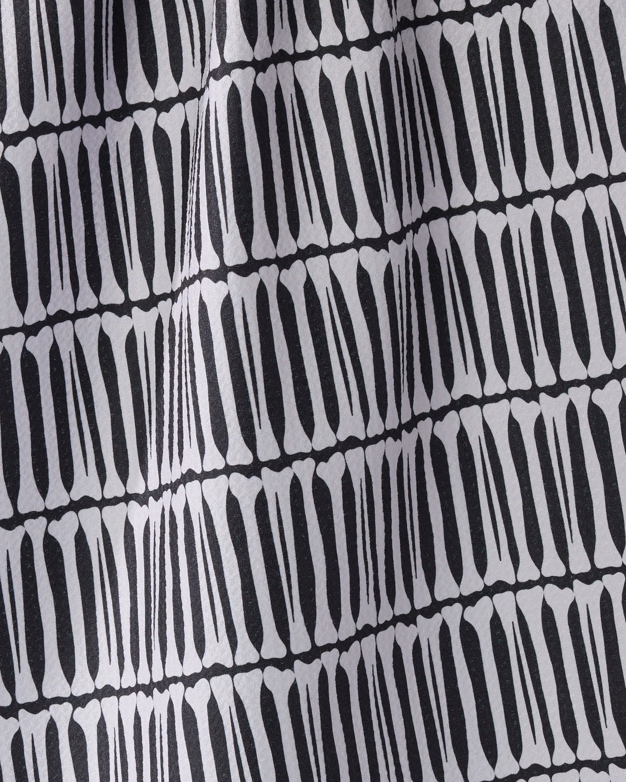 A close-up of Geometry's Rattler tea towel, ultra-absorbent and crafted from recycled materials, shows its black and white geometric pattern of elongated vertical shapes on a light background with a slightly wrinkled texture.
