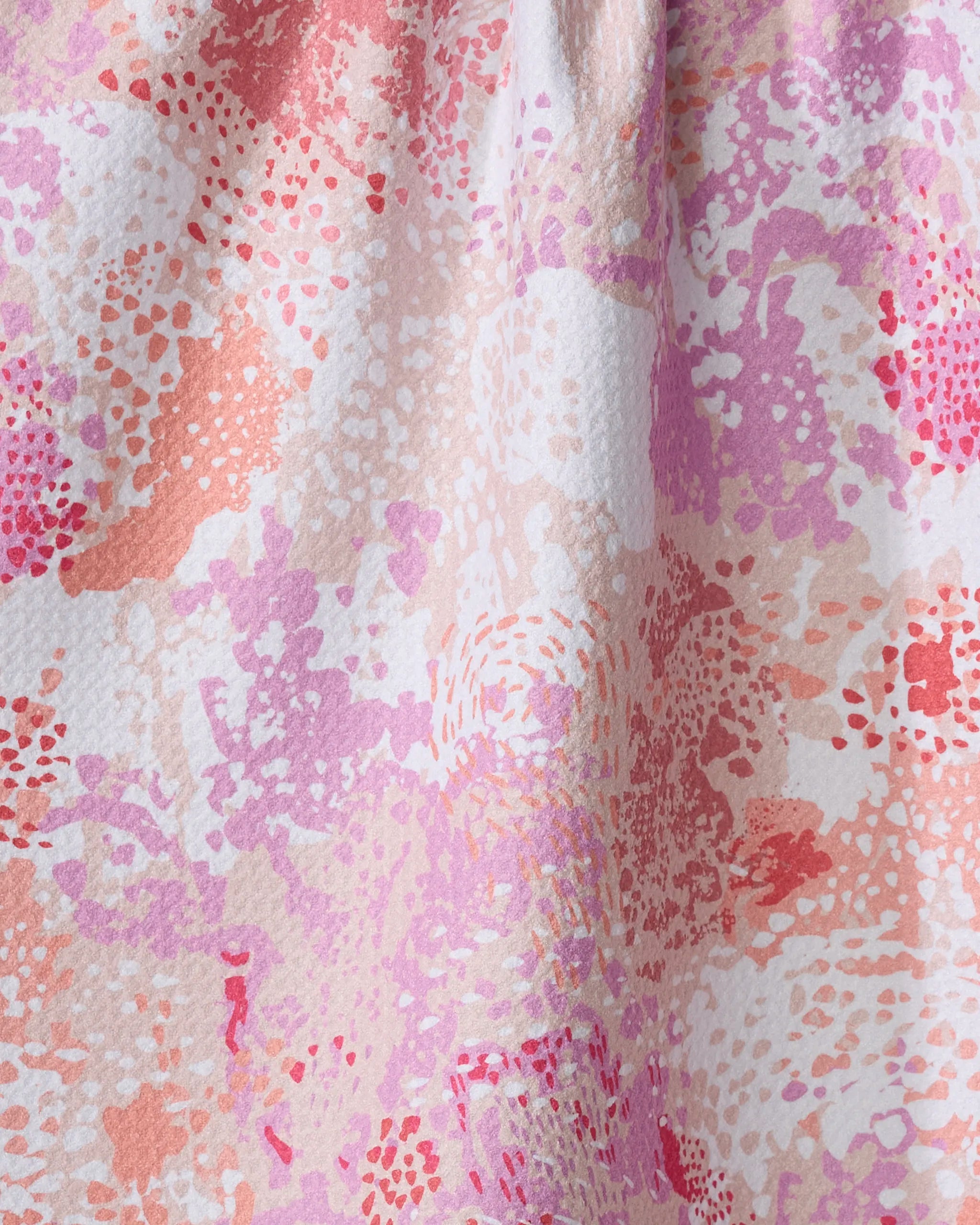 Abstract close-up of Rawhide, an absorbent dish towel by Elisabeth Wing, featuring a colorful, irregular pattern in pink, peach, red, lavender, and white with textured dotted and blotchy areas.