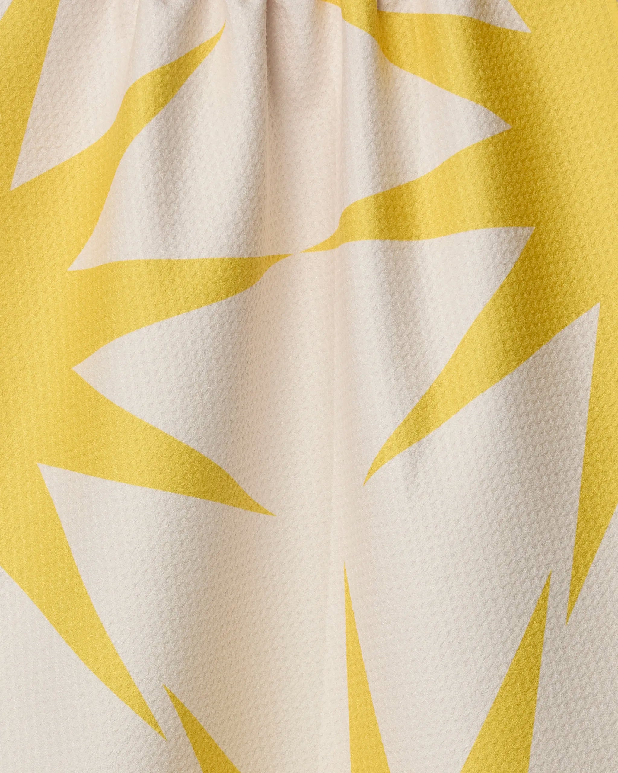 Close-up of Geometry's "Ray" tea towel, made from recycled materials, featuring a bold yellow and white sunburst pattern with jagged shapes on a light background.