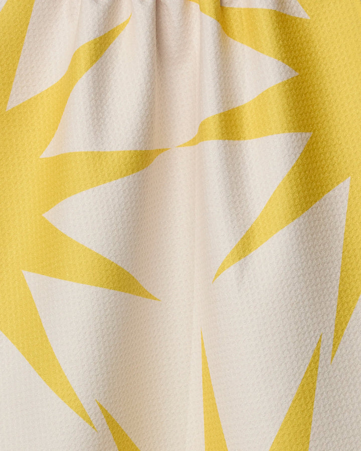 Close-up of Geometry's "Ray" tea towel, made from recycled materials, featuring a bold yellow and white sunburst pattern with jagged shapes on a light background.