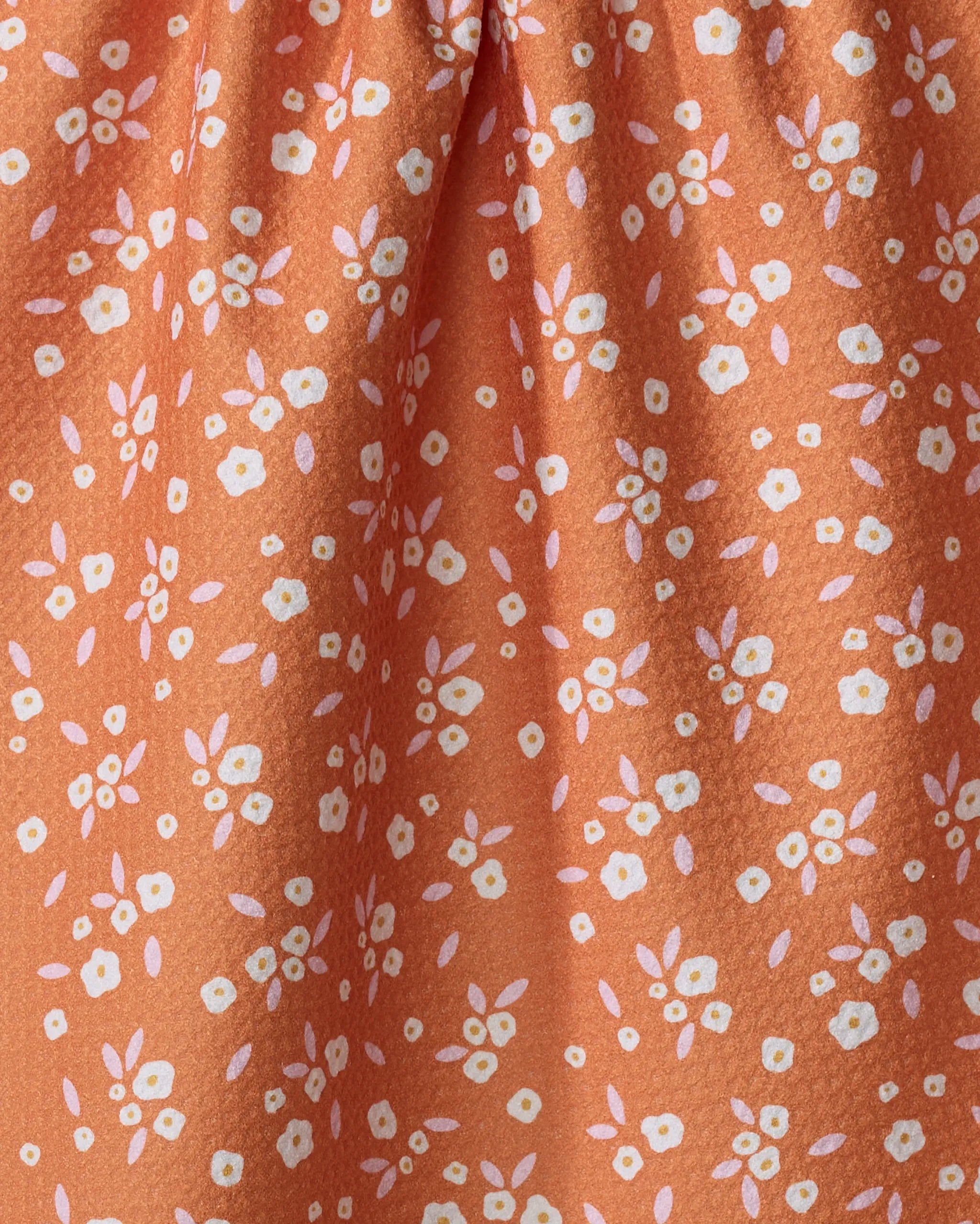 Close-up of the "Red Field of Flowers" dish towel by Megan Roy, featuring a textured orange fabric adorned with small white floral and leaf patterns. The material is softly gathered at the top, highlighting its absorbent quality.
