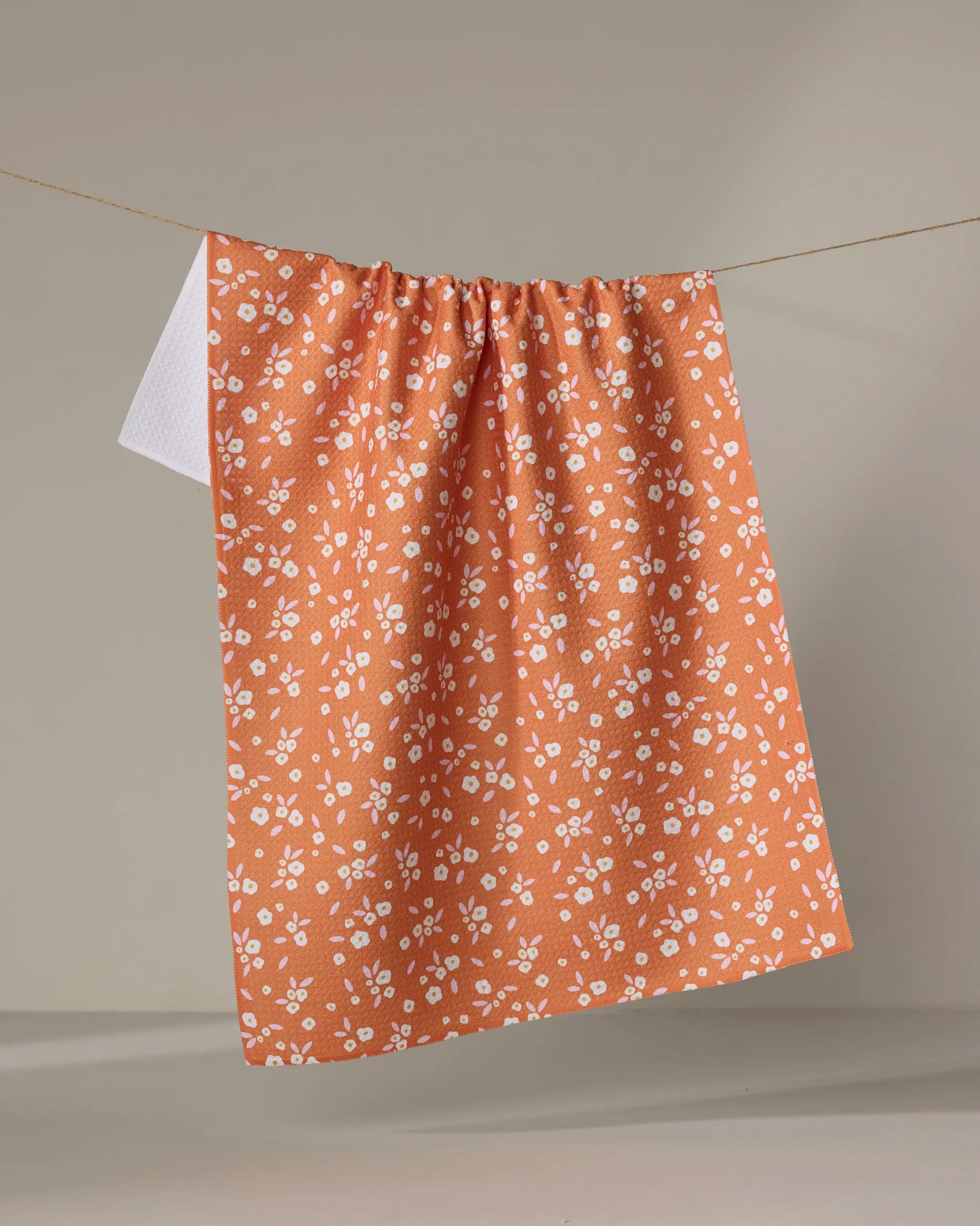 The Megan Roy "Red Field of Flowers" absorbent dish towel hangs on a string against a plain beige background.