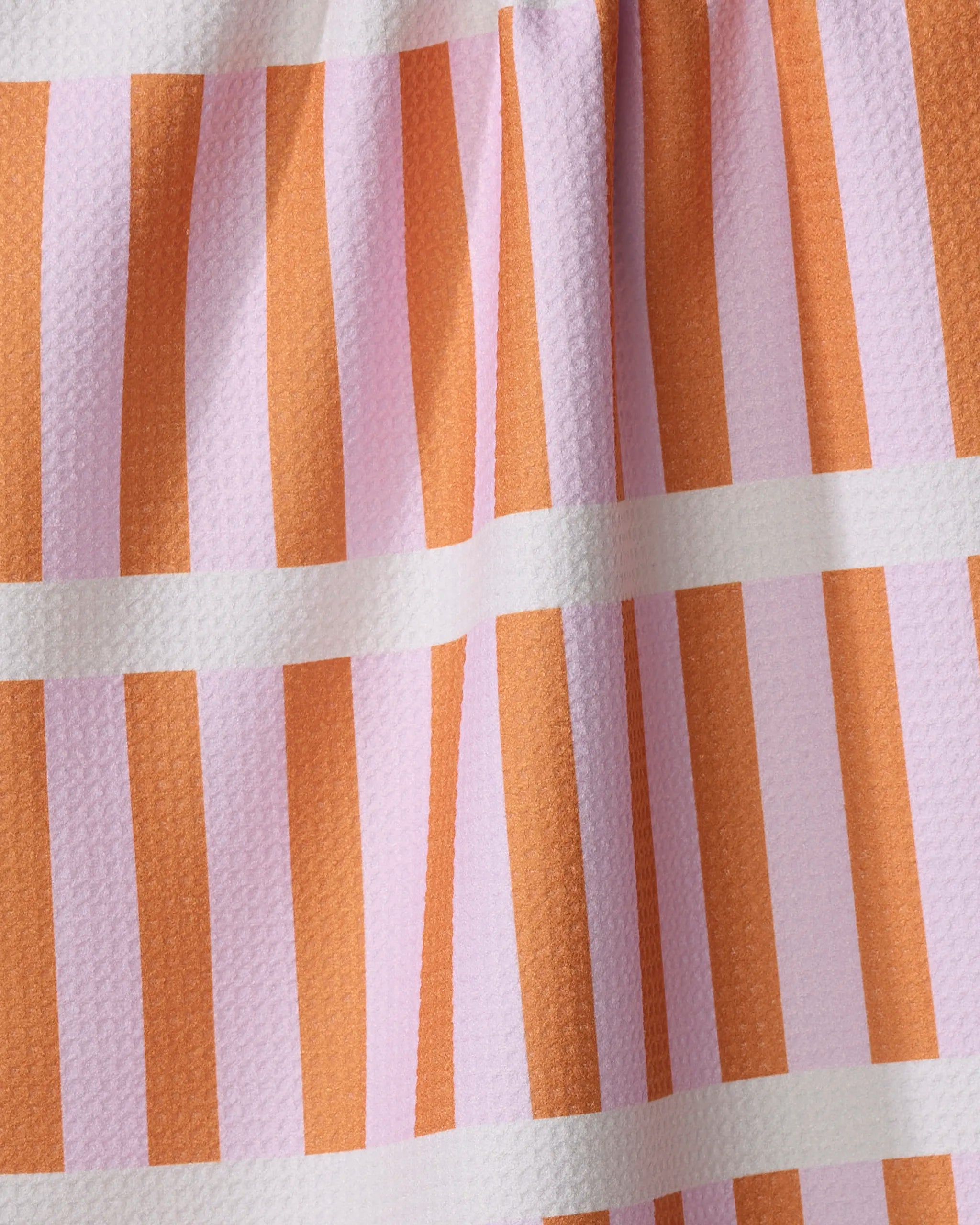 A close-up of Happy Hemera’s Red Glow kitchen towel, crafted from recycled materials, shows vertical orange and light pink stripes with white horizontal lines and a textured, gently folded surface.