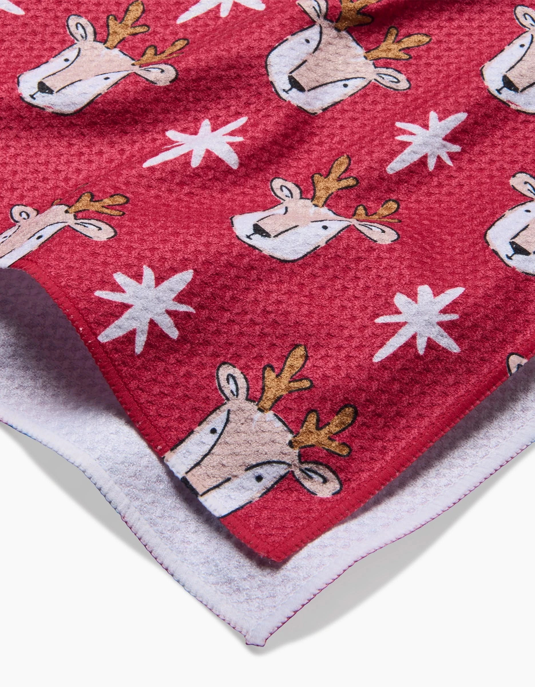 The Hufton Studio Reindeer Star tea towel features red textured fabric with cartoon reindeer faces, white stars, and a white terry cloth backing, made from quick-drying recycled materials.