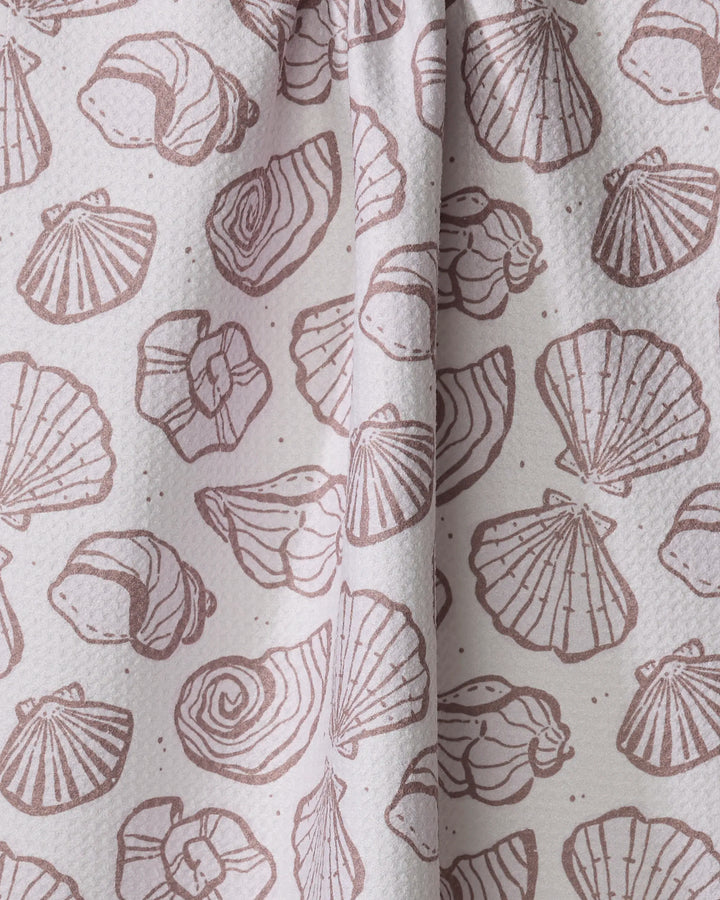 Close-up of Teri the Butter's Retro Coastal Seashells in Neutral tea towel, ultra-absorbent and made from recycled materials, featuring a repeated pattern of light brown seashells on a pale, textured background.
