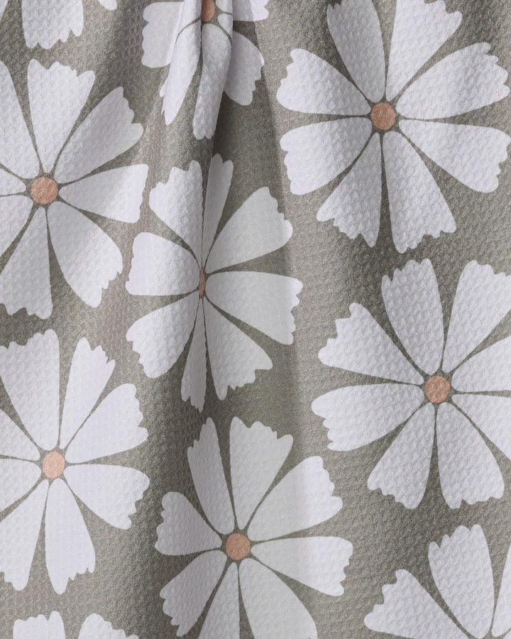 The Retro Daisy kitchen tea towel by Hufton Studio features a textured, slightly wrinkled fabric made from recycled materials, and showcases a repeating pattern of large white daisy-like flowers with light brown centers on a muted gray-green background.