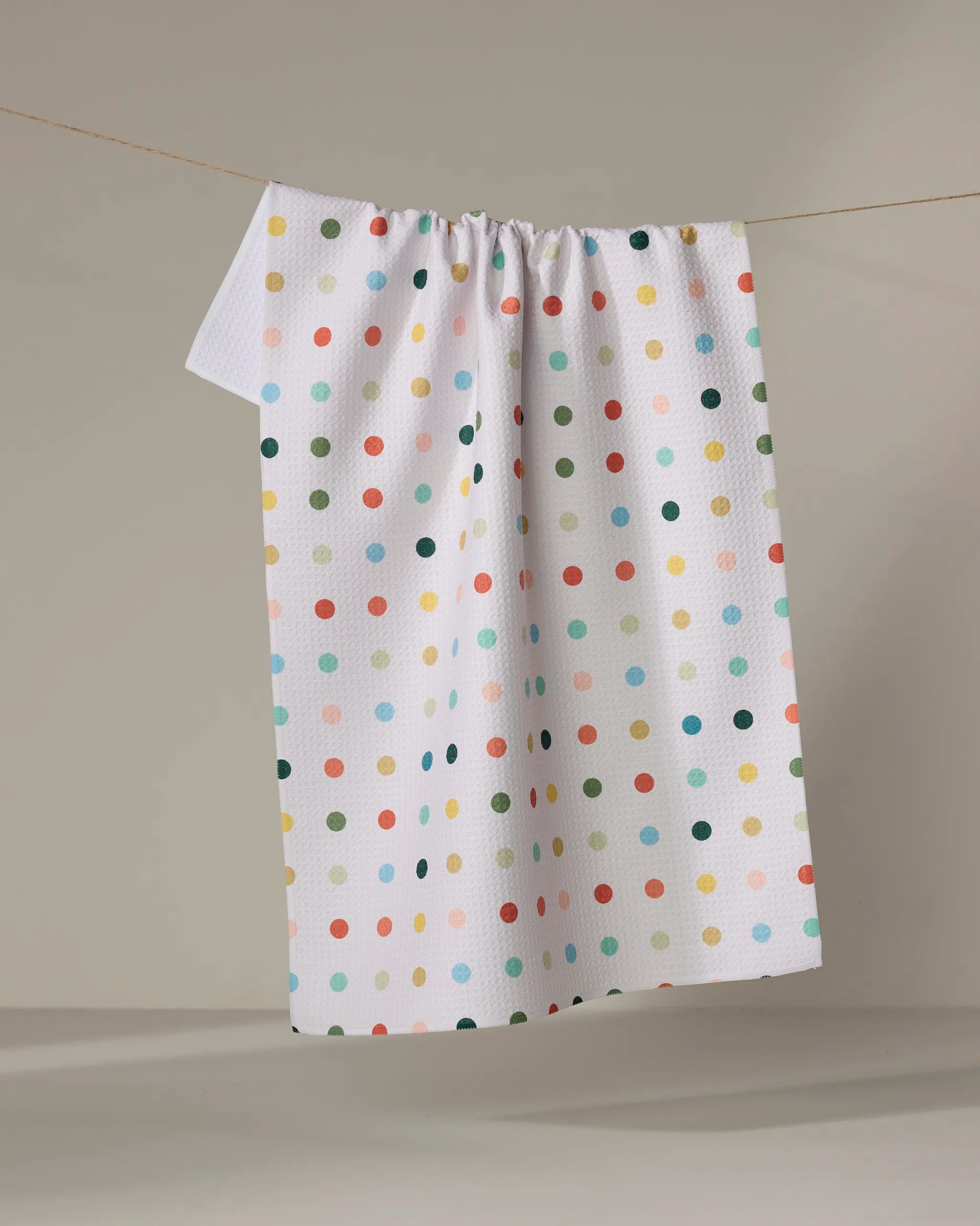 The Elizabeth Edwards Retro Dot towel, featuring colorful polka dots on a white ultra-absorbent fabric, hangs on a thin string against a neutral background.