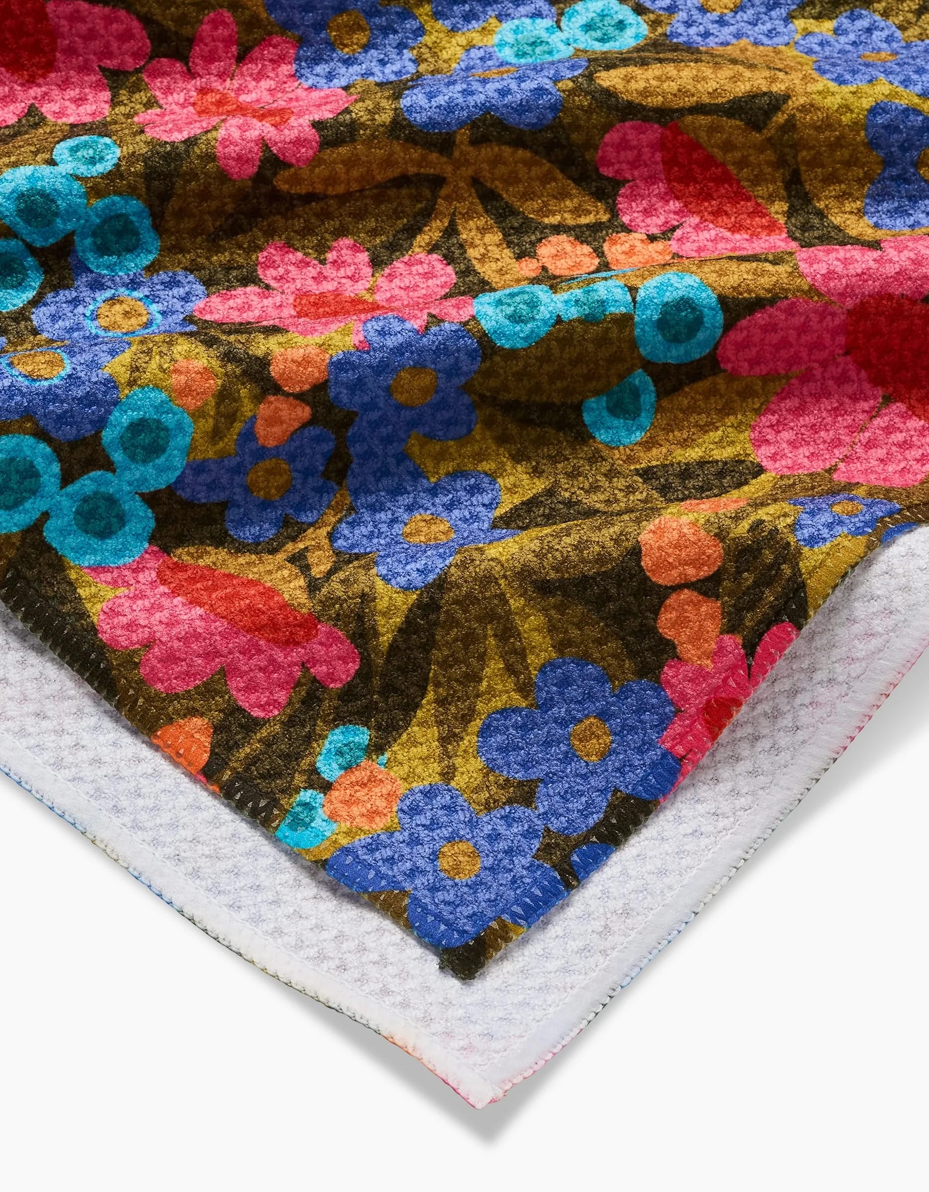 A close-up of Lisa Nelson’s Retro Garden tea towel shows its vibrant blue, pink, and red floral pattern on brown, plus a peek at the ultra-absorbent Geoweave front and white waffle-textured reverse at the corner.