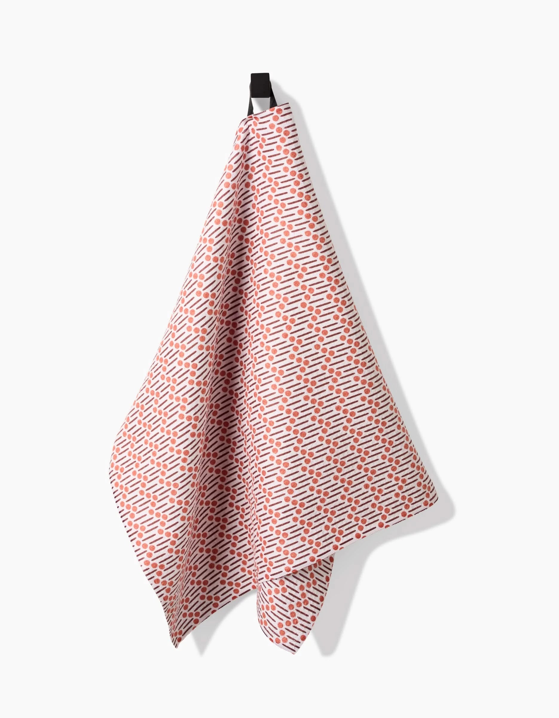 A Teri the Butter Retro Geo tea towel, crafted from recycled materials and displaying a red and blue repeating pattern, hangs from a black hook against a plain white background.