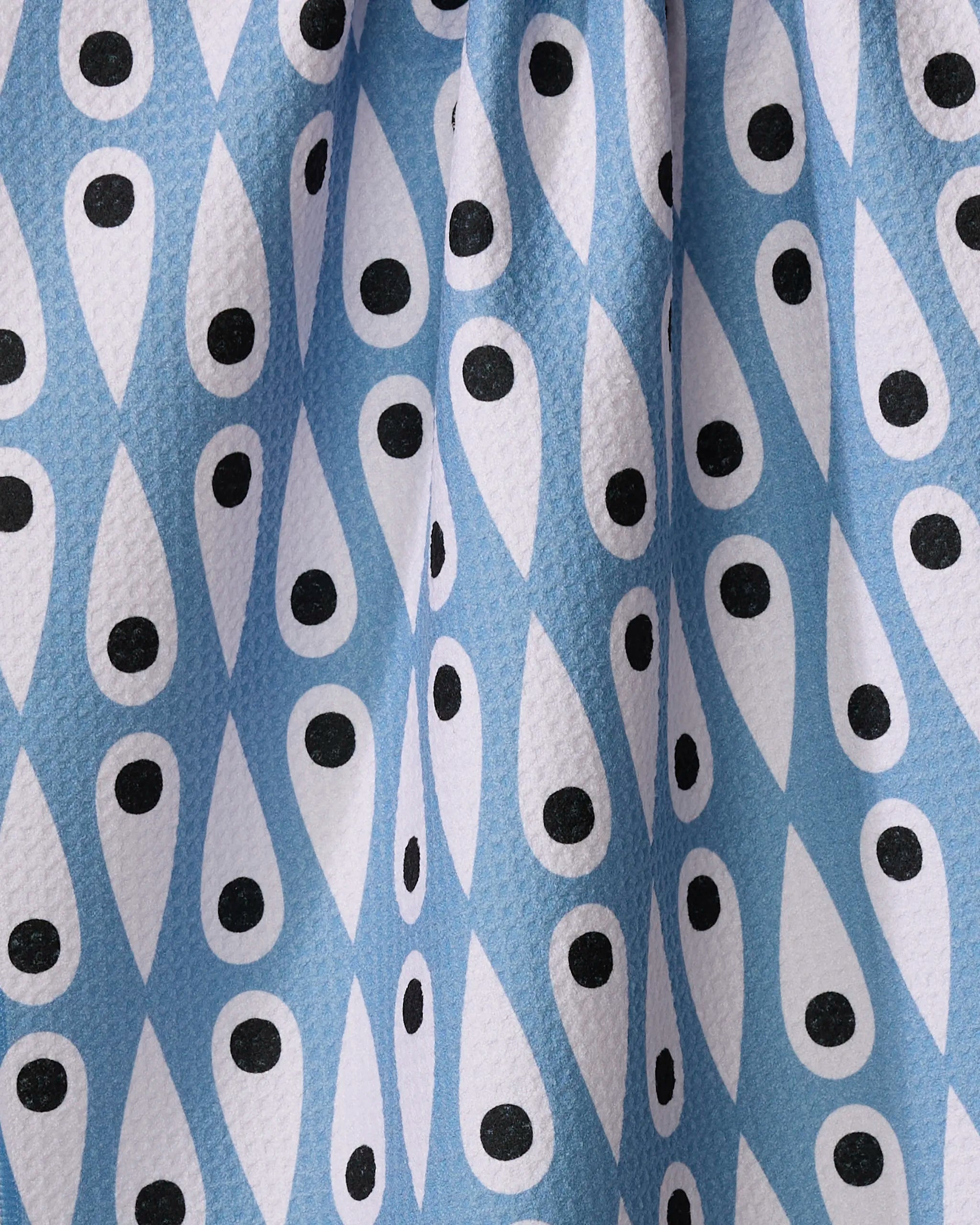 A close-up of the Retro Rain tea towel by Anette Heiberg shows its blue and white teardrop pattern with black dots, creating an eye-like geometric design on slightly textured recycled fabric—ideal for eco-friendly kitchens.