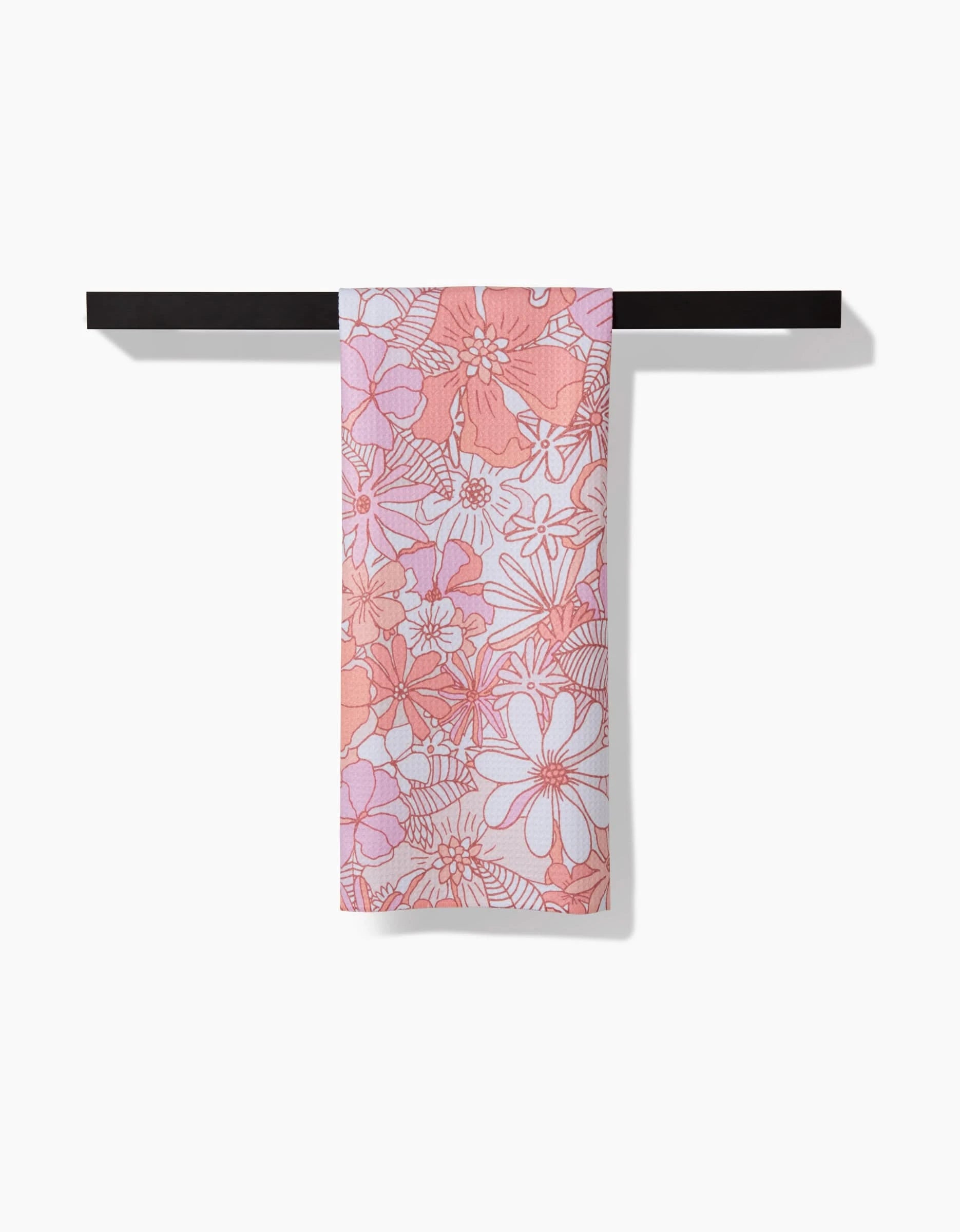 The Retro Vibes tea towel by Marina Solodka, featuring a pink and white floral pattern in soft Geoweave fabric, hangs neatly folded over a black towel bar against a white background.