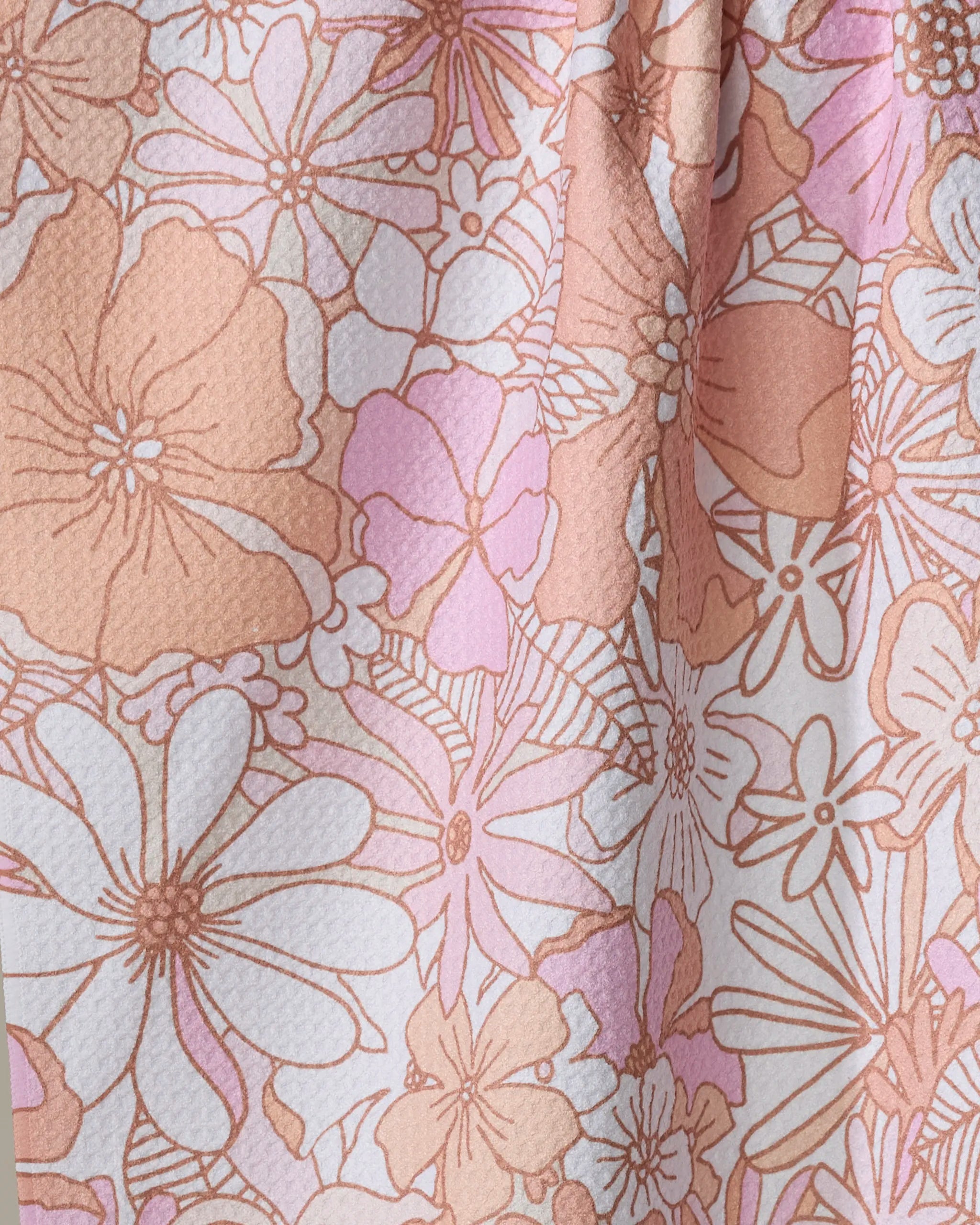 A close-up of Marina Solodka's Retro Vibes kitchen tea towel, made from recycled materials, shows detailed pink, peach, and white vintage floral patterns on textured fabric.