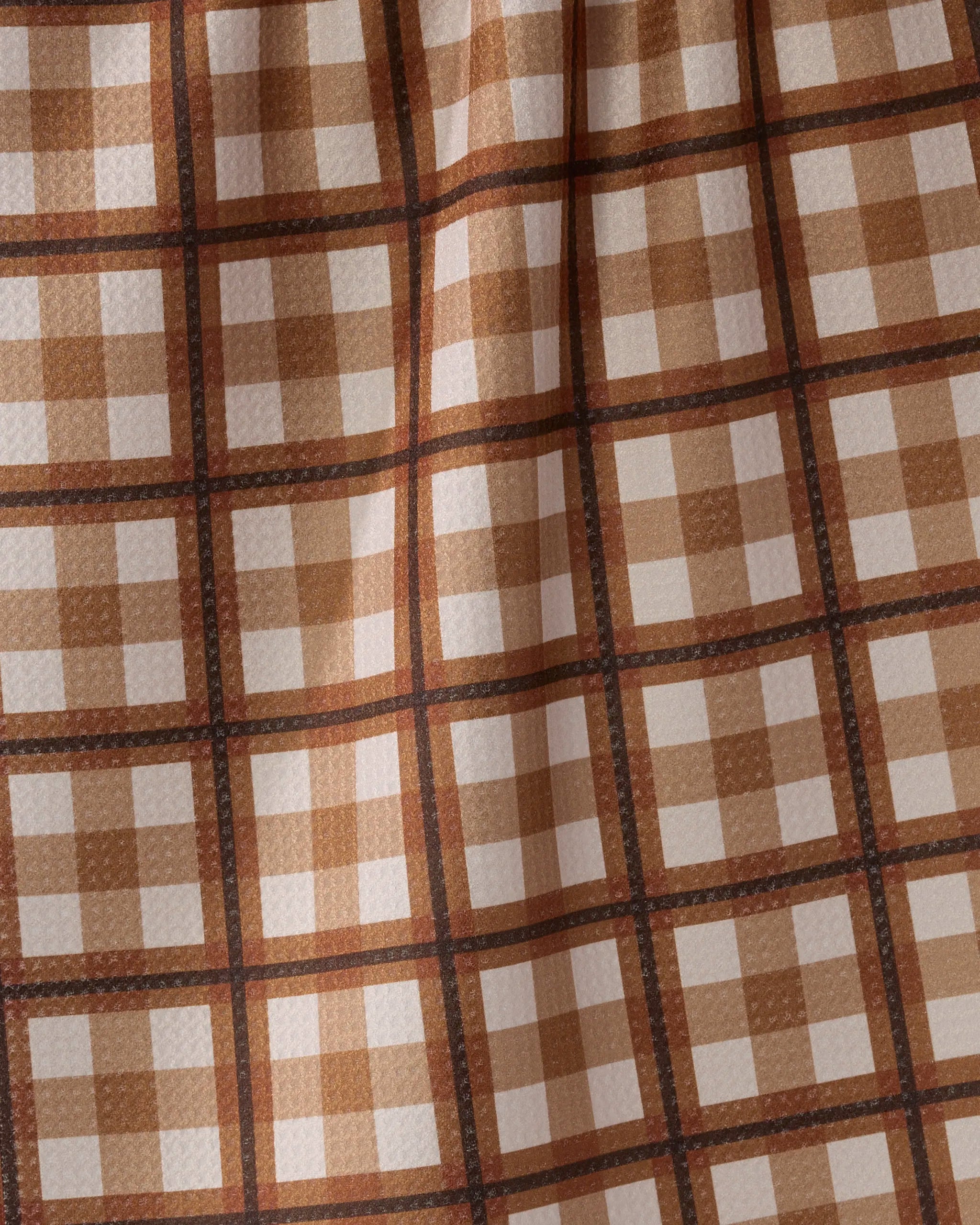 A close-up of Geometry's Rich Cocoa tea towel in brown, beige, and cream plaid. Its slightly textured fabric has soft folds and subtle shadows, crafted from recycled materials for an eco-friendly touch.