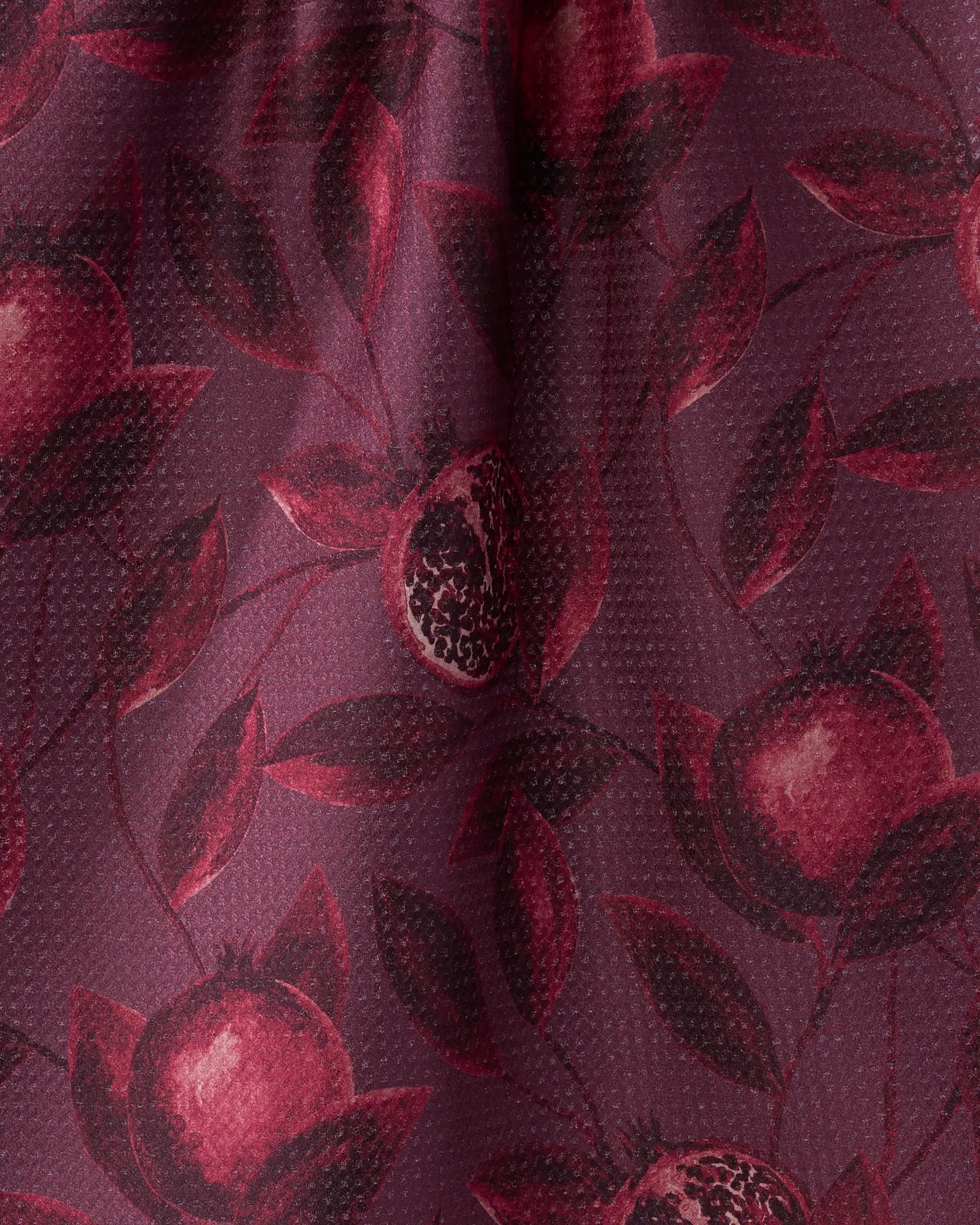 A close-up of the Geometry "Rich Garnet" tea towel, showcasing a repeating pomegranate and leaf pattern in dark red and burgundy on slightly shiny, textured fabric.