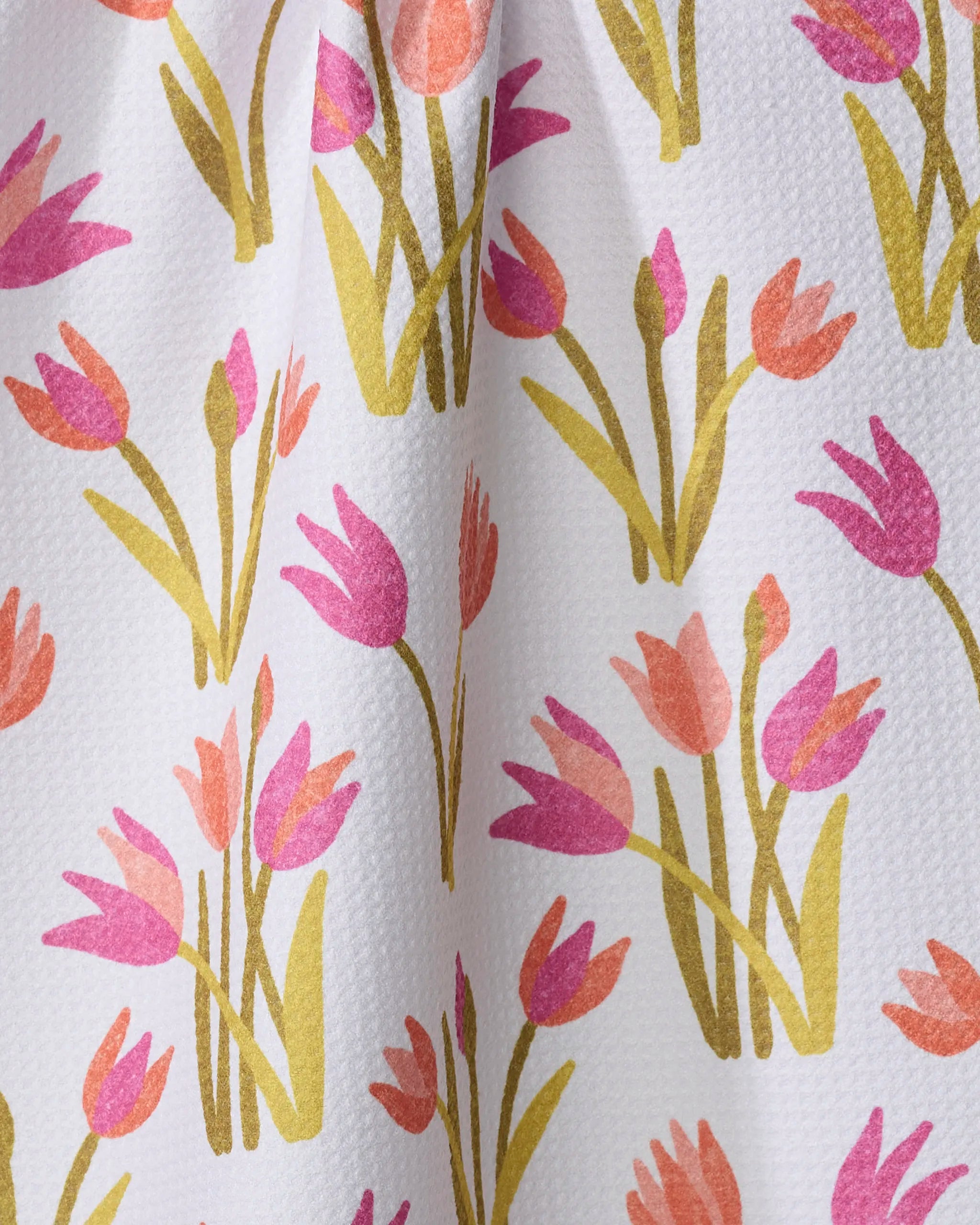 A close-up of the Riley dish towel by Amy MacCready: white, textured fabric with a repeating pattern of pink, coral, and gold stylized tulips with green stems—an absorbent and colorful tea towel for your kitchen.