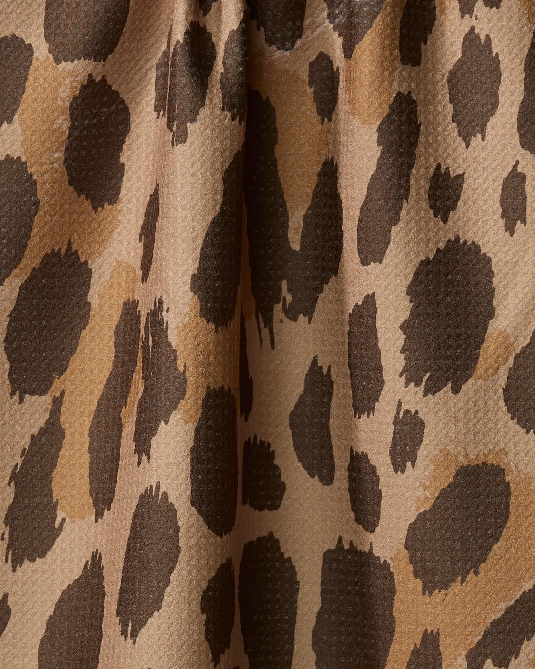 Close-up of the Geometry Roam absorbent dish towel, featuring a leopard print with irregular dark brown and black spots on a light tan, textured fabric—perfect for adding flair to your kitchen essentials.