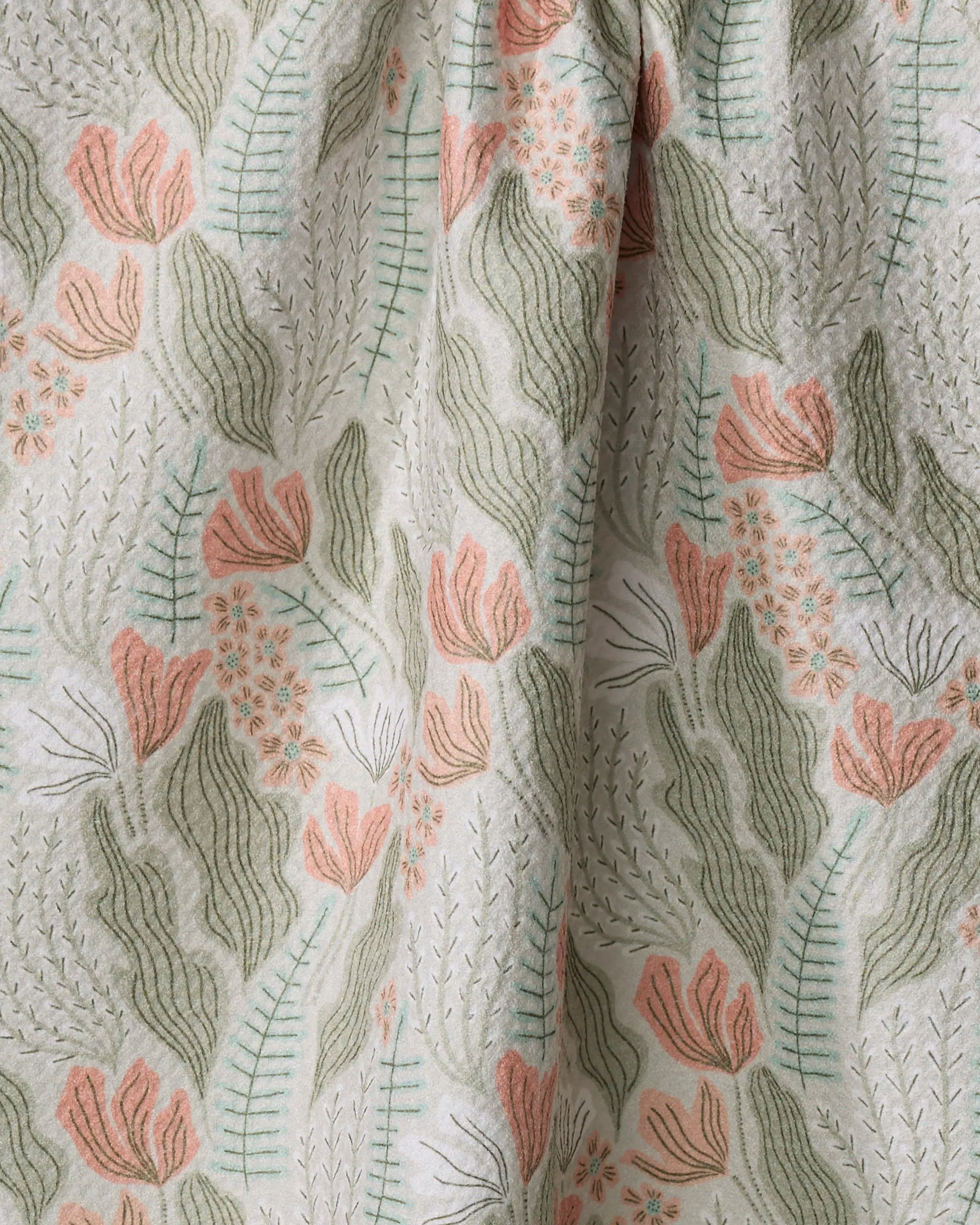 A close-up of the Rollie quick-drying towel by Amy MacCready, featuring an embroidered floral pattern with light green leaves and pink flowers on a white background. The delicate stitching and soft pastel hues stand out beautifully.