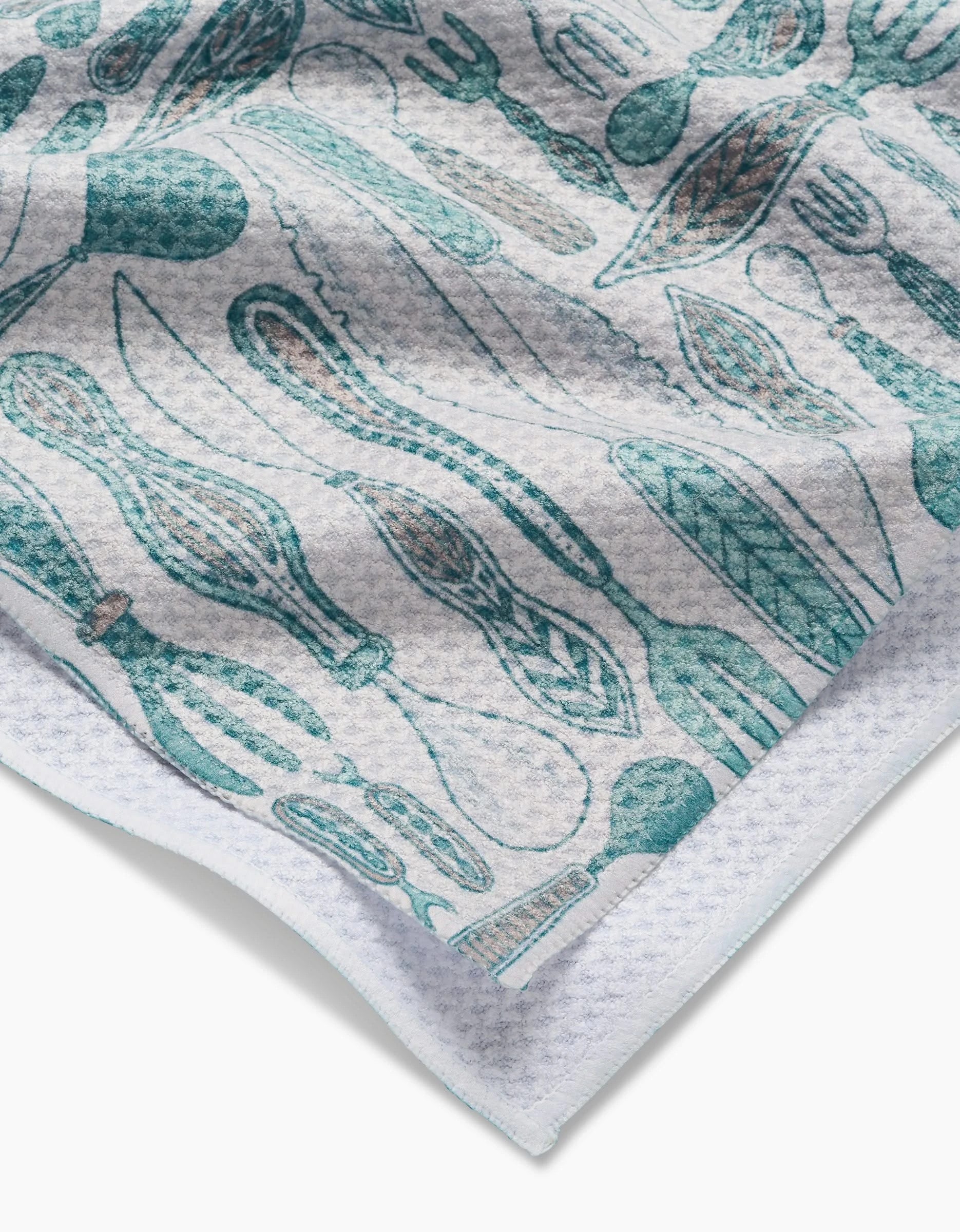 A close-up of the Romy kitchen towel by Amy MacCready, featuring a teal utensil pattern with forks, spoons, and whisks. The Geoweave fabric looks textured, ultra-absorbent, and soft.