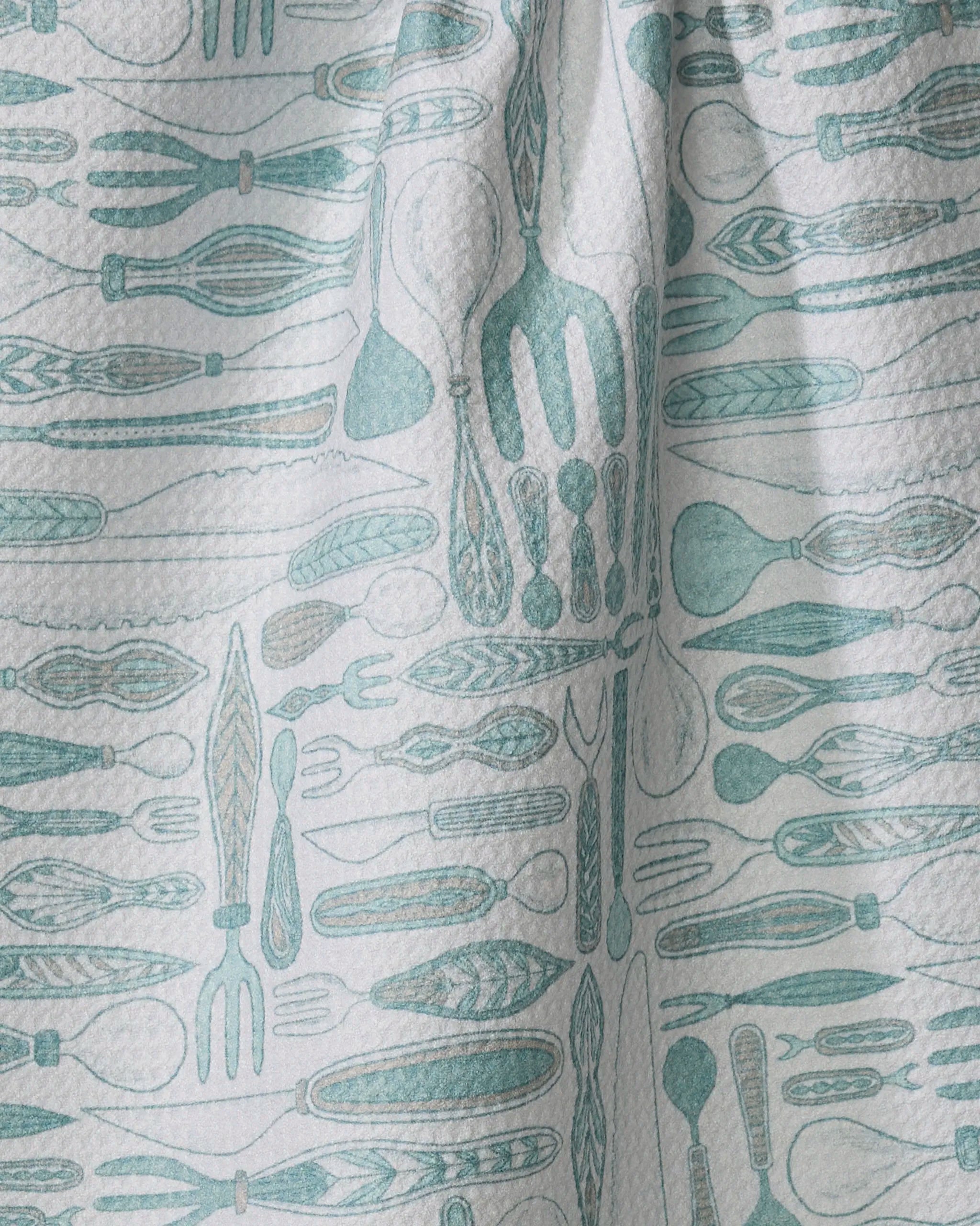The Romy dish towel by Amy MacCready is a textured white absorbent towel with teal and light blue kitchen utensils—forks, spoons, whisks, and knives—arranged in horizontal rows.