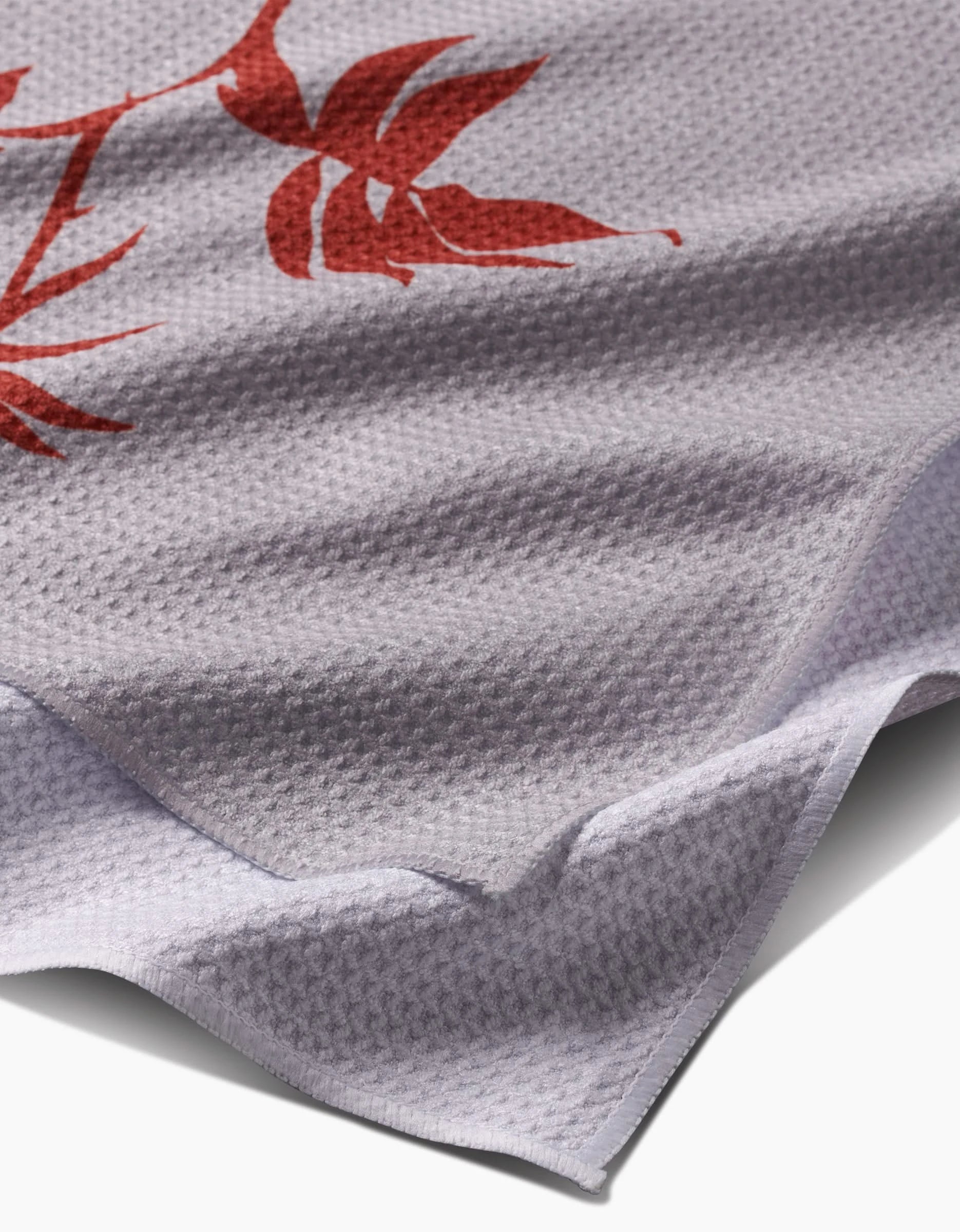 Close-up of the Rose tea towel by PrintedPlant, featuring a red floral pattern on light gray Geoweave Fabric with a waffle weave texture and neatly hemmed edges.