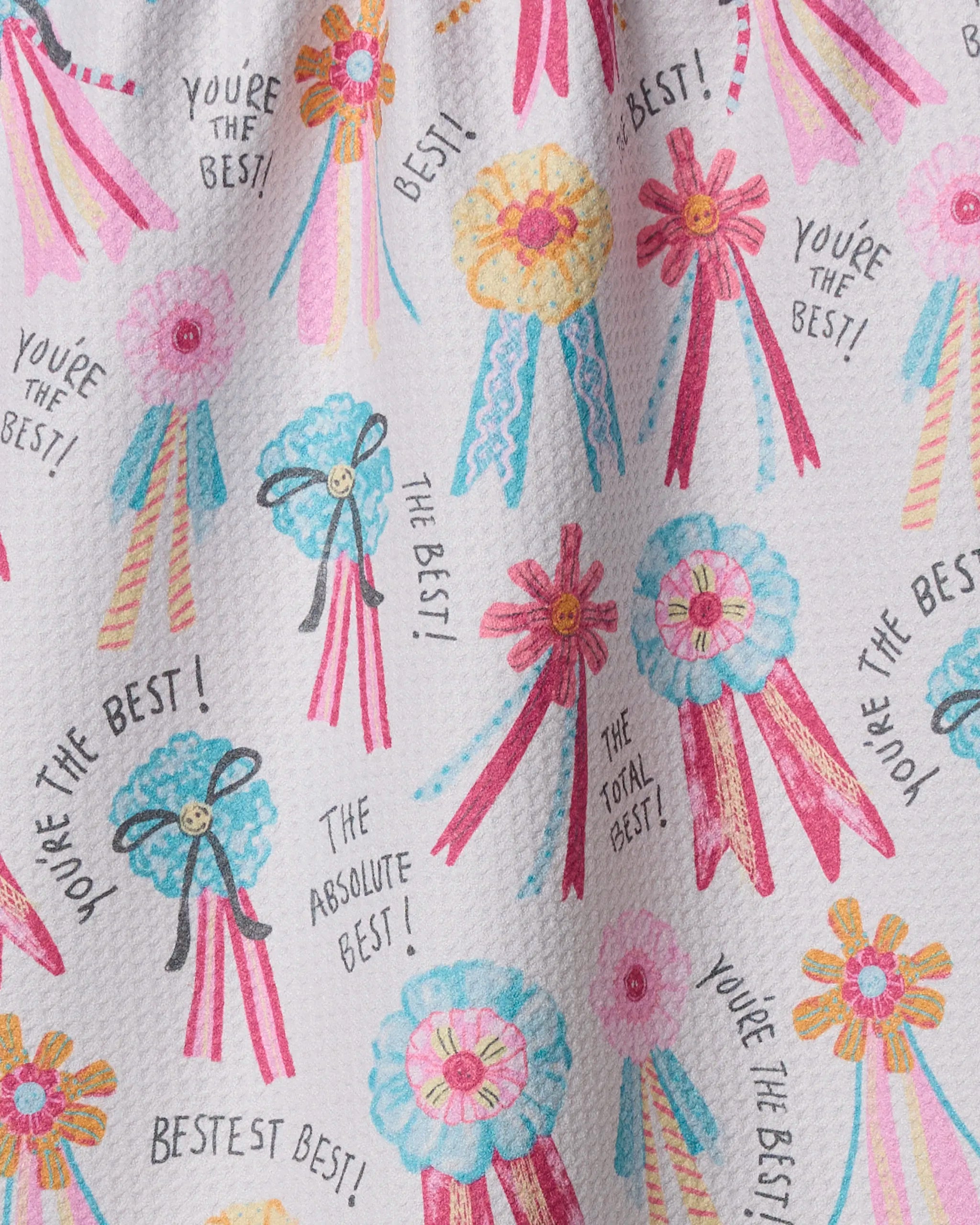 Rosettes for You by Geometry is a patterned tea towel with colorful pink, blue, and yellow award ribbons and phrases like "You're the best!" Made from quick-drying recycled materials.