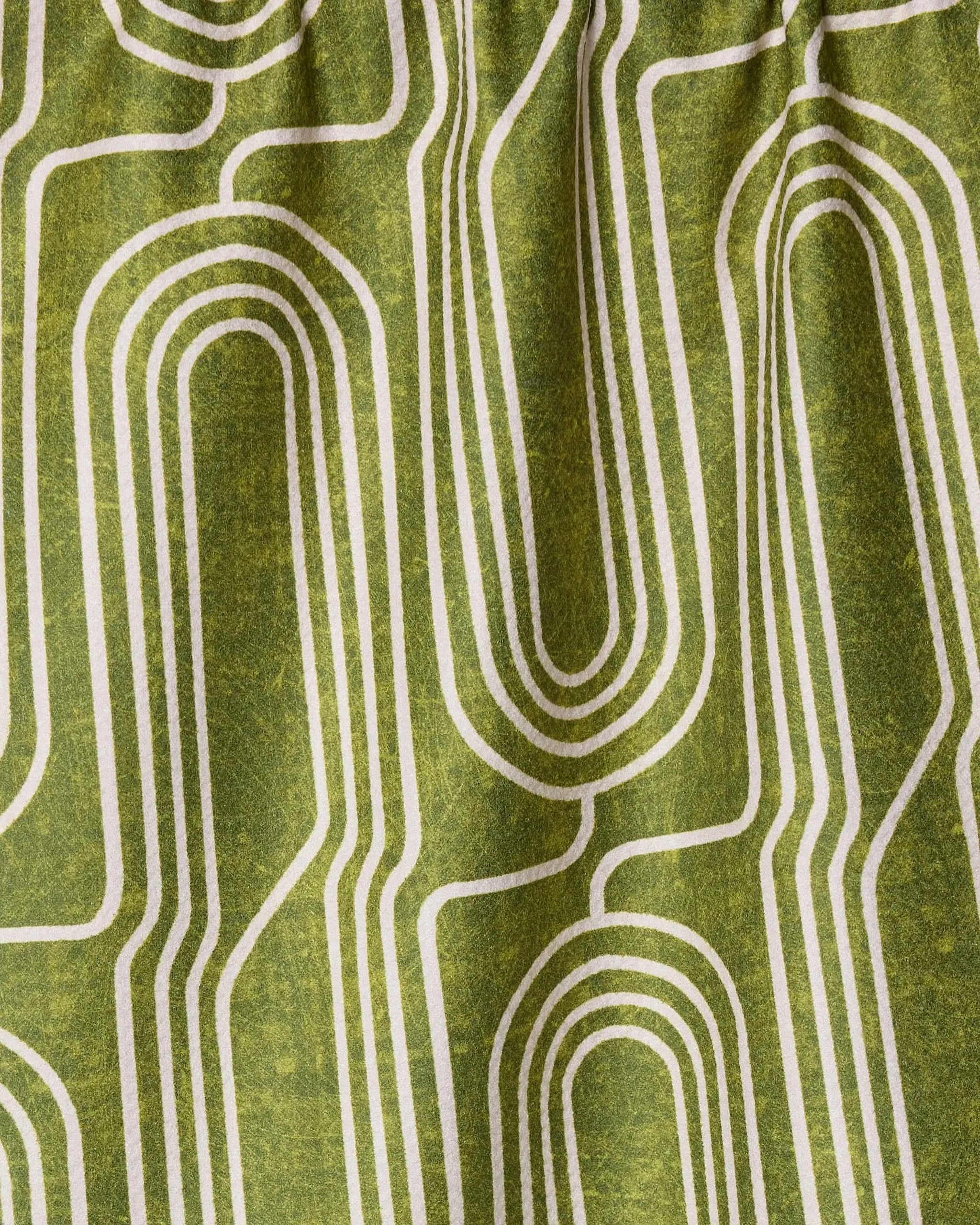Roslyn by Amy MacCready is a green fabric crafted from recycled materials, featuring a retro white geometric pattern of curved, parallel lines in a repeating maze-like design. The fabric is slightly gathered at the top.