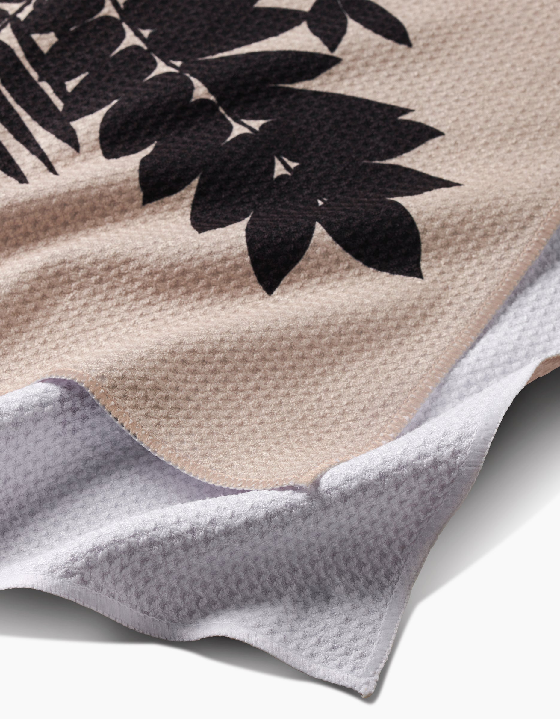 A close-up of the Rowan tea towel by PrintedPlant, featuring ultra-absorbent beige Geoweave fabric with a black leaf pattern, white underside, wavy edge, and intricate detailing—an ideal addition to any collection.