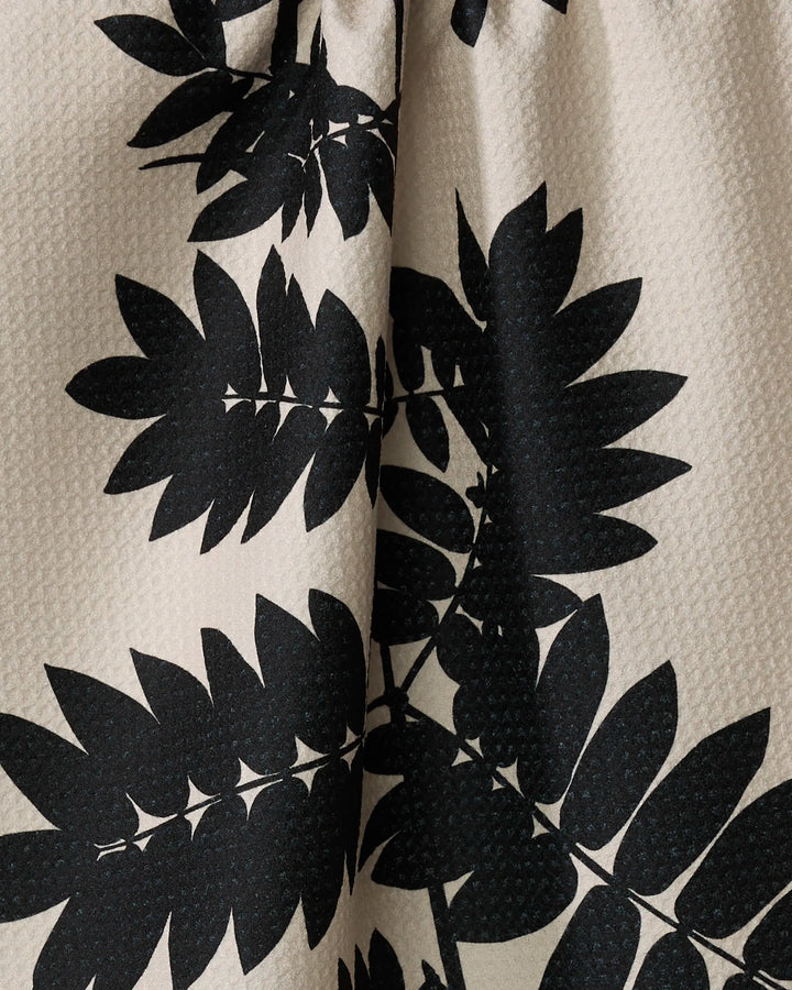 The Rowan kitchen towel by PrintedPlant features ultra-absorbent, recycled beige fabric with a bold black leafy plant design. Large overlapping leaves create a striking contrast against the textured light background.