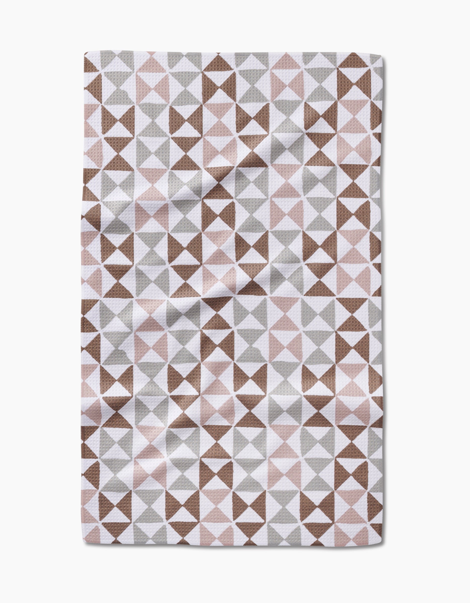 The Rubix tea towel by Studio Jeannot features a geometric triangle pattern in brown, gray, and light pink on Geoweave fabric made from recycled materials, shown with subtle creases against a white background.