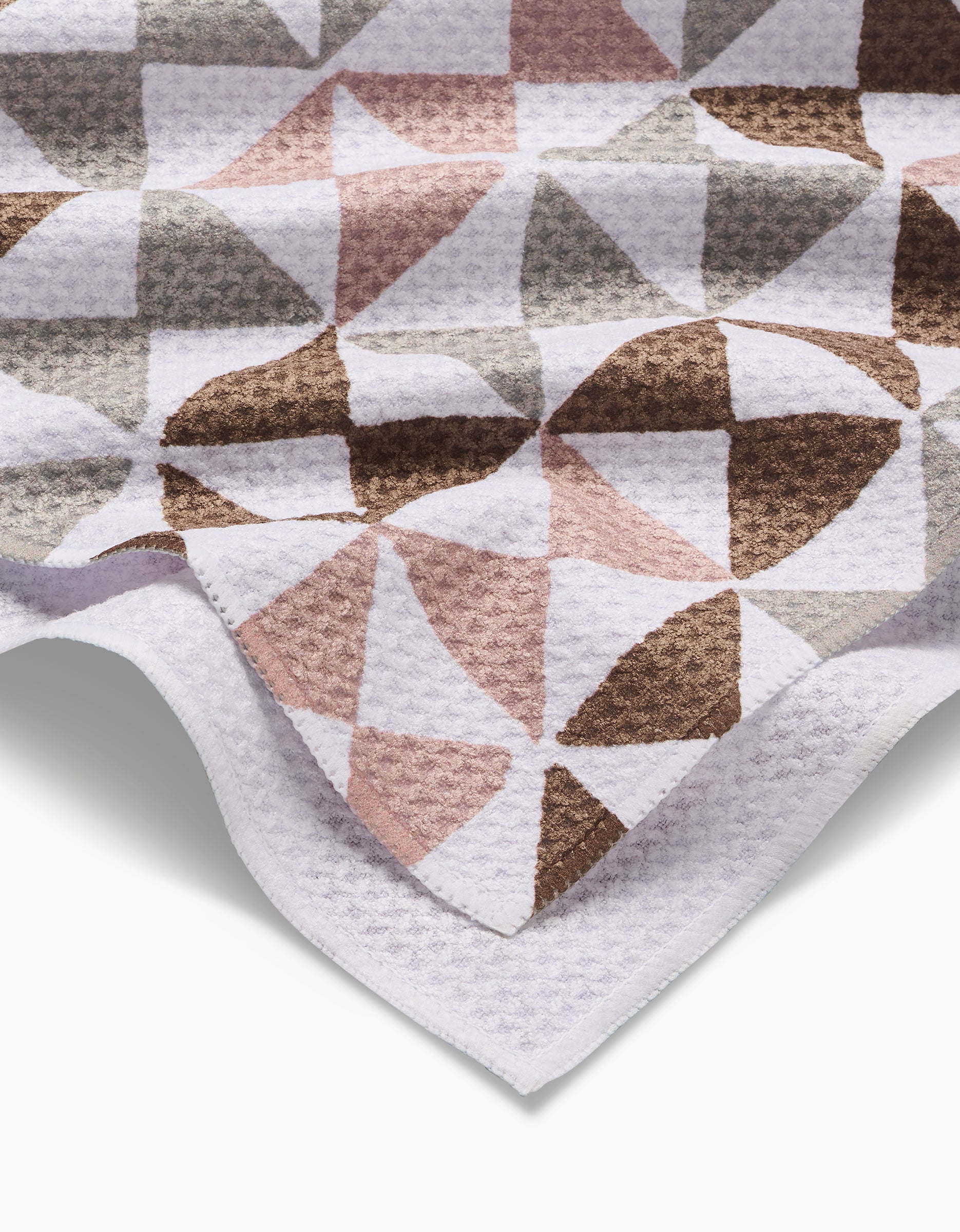The Rubix tea towel by Studio Jeannot showcases a geometric pattern of overlapping semi-circles in muted brown, pink, gray, and white tones. Made from recycled materials, it features a crisp white border along the edge.