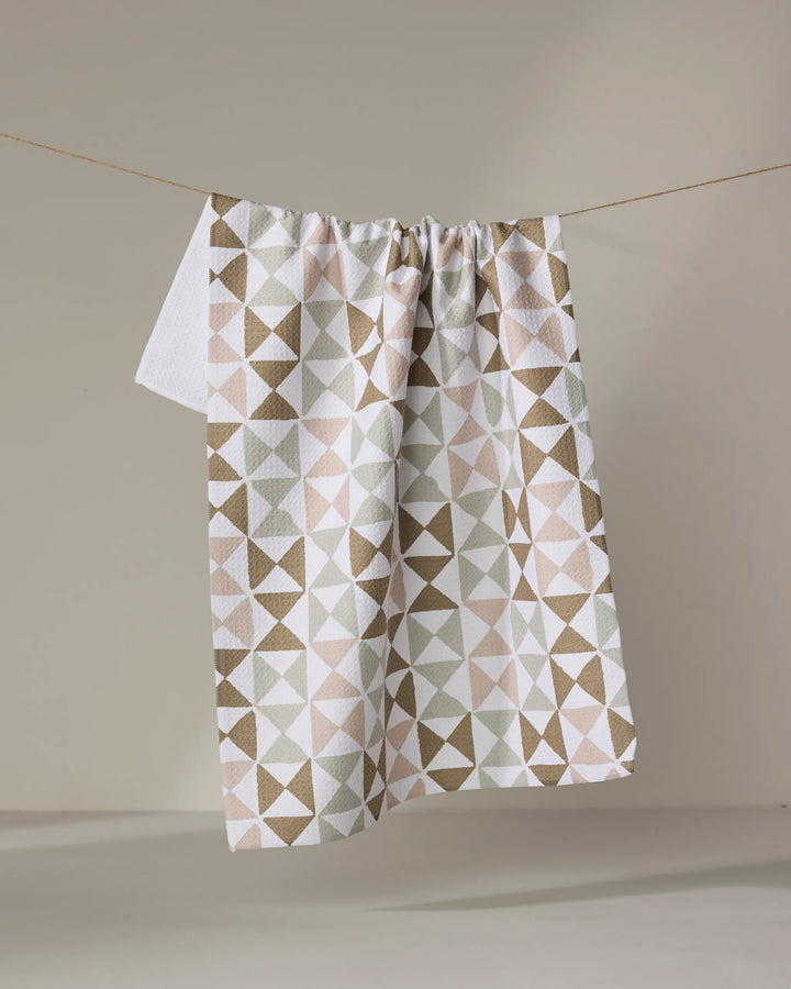 The Rubix tea towel by Studio Jeannot, featuring a geometric pattern in beige, brown, and white, hangs on a clothesline against a neutral background.