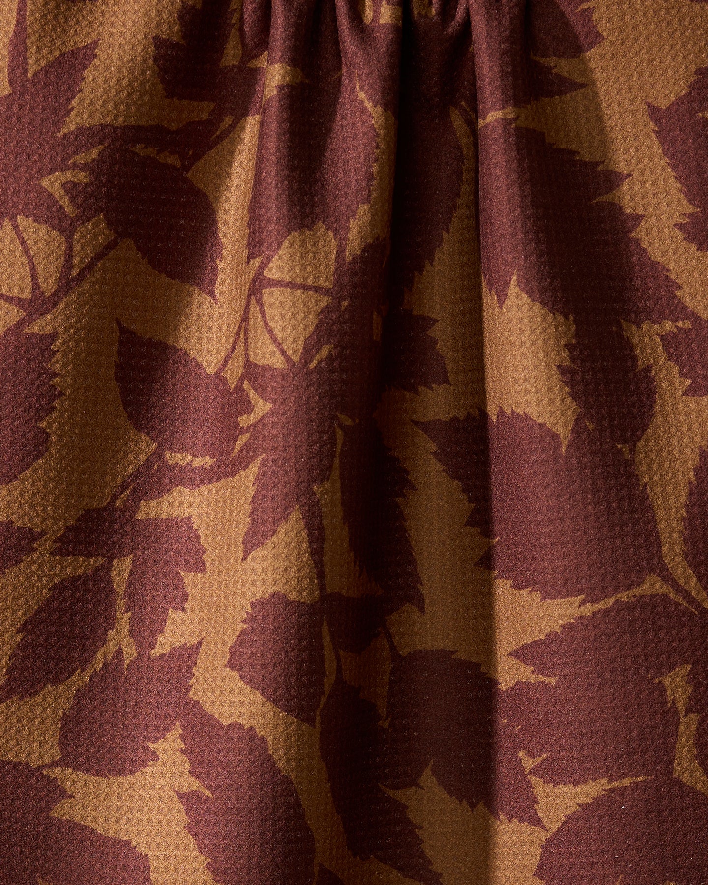 Close-up of Geometry’s Rustle tea towel, made from recycled materials, showing textured fabric with a brown and dark red leaf pattern. The towel is gently gathered at the top, creating soft folds and shadowed details.