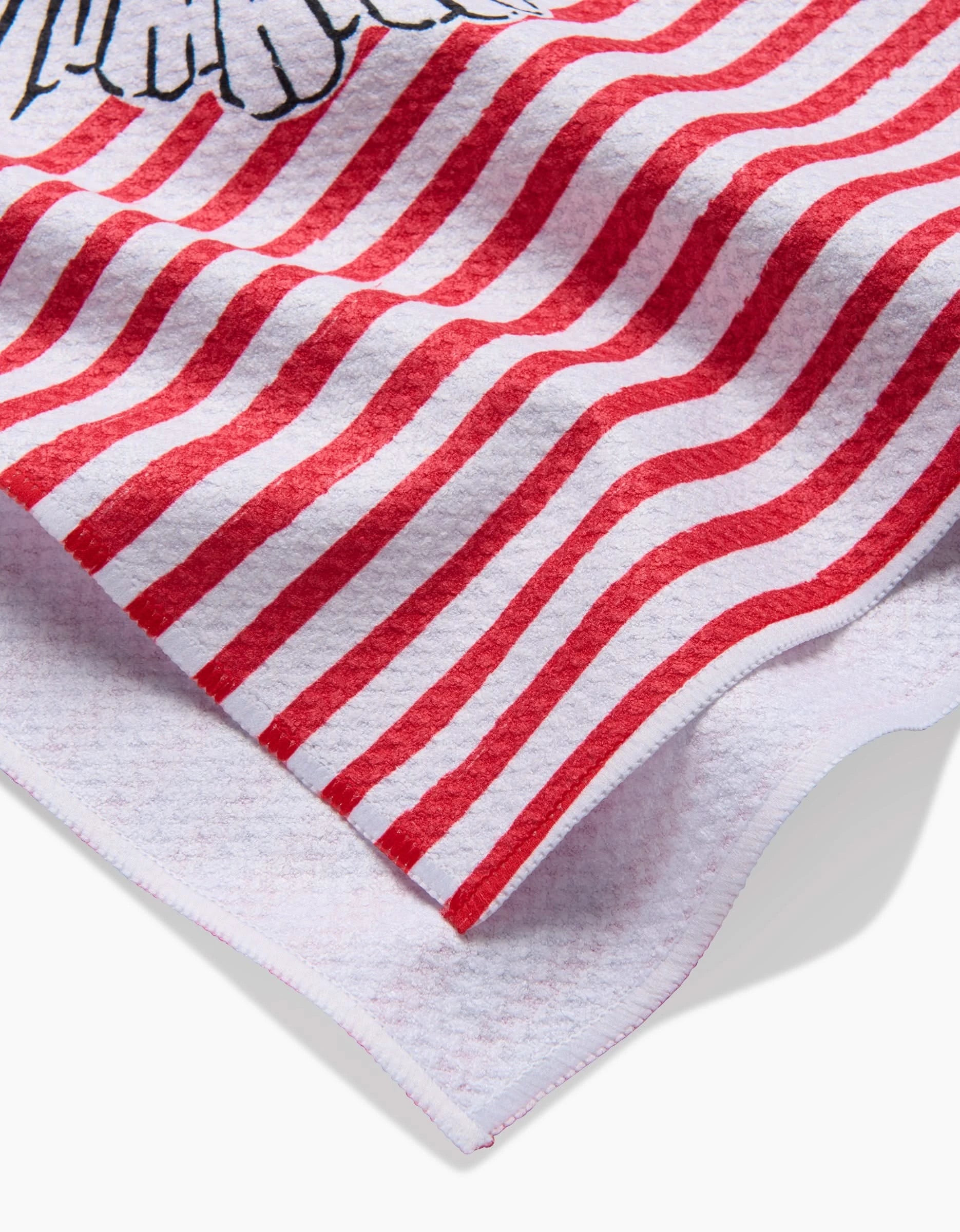 A close-up of the Hufton Studio Sacred Striped Love Hearts tea towel, showing its red and white wavy stripes, part of a black and white illustrated edge design, and textured ultra-absorbent fabric softly folded.