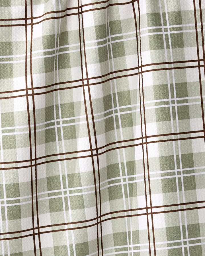 A close-up of the Sage Season tea towel by Ashley Reeves shows its green and white plaid with brown lines forming squares. Made from recycled materials, this textured fabric is quick-drying and ideal for everyday use.