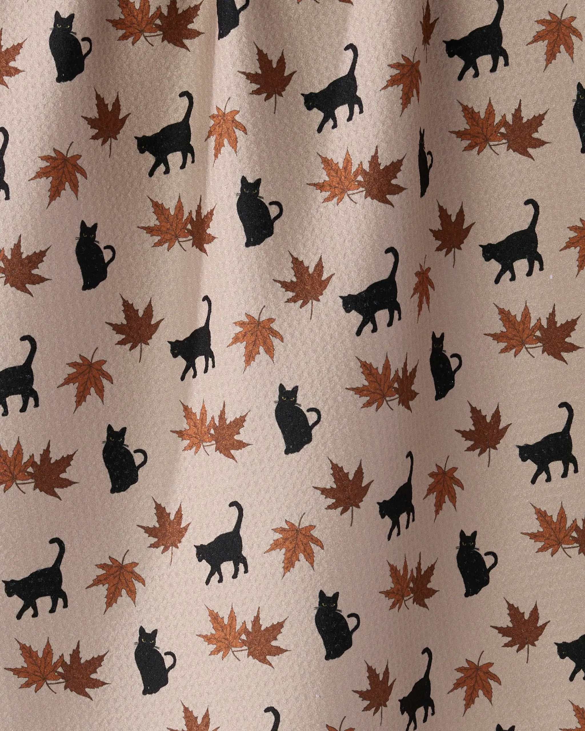 The Salem Woods kitchen towel by Geometry features black cat silhouettes and brown maple leaves on beige, crafted from recycled materials.