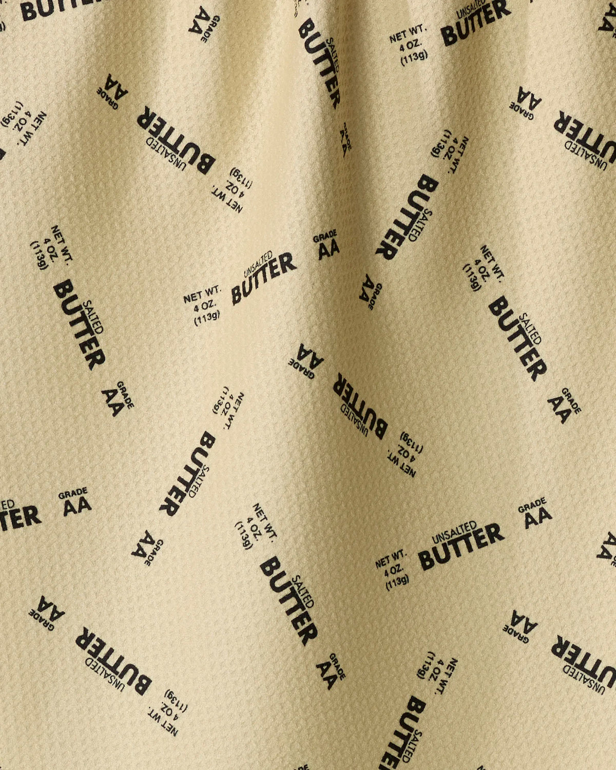 A tan GEOMETRY Salted vs Unsalted quick-drying tea towel with a repeating pattern of Butter, Salted, Unsalted, Grade AA, and Net wt. 4 oz.