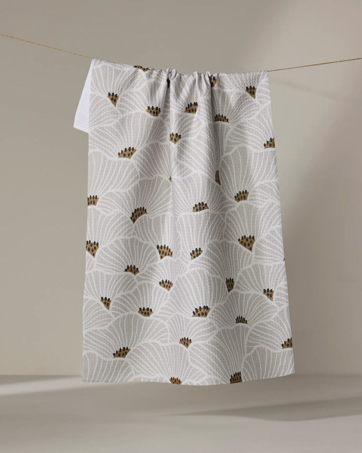 The "San Diego" tea towel by Amy MacCready features white absorbent fabric with light gray fan patterns and small brown dot clusters, shown hanging from a string against a neutral background.